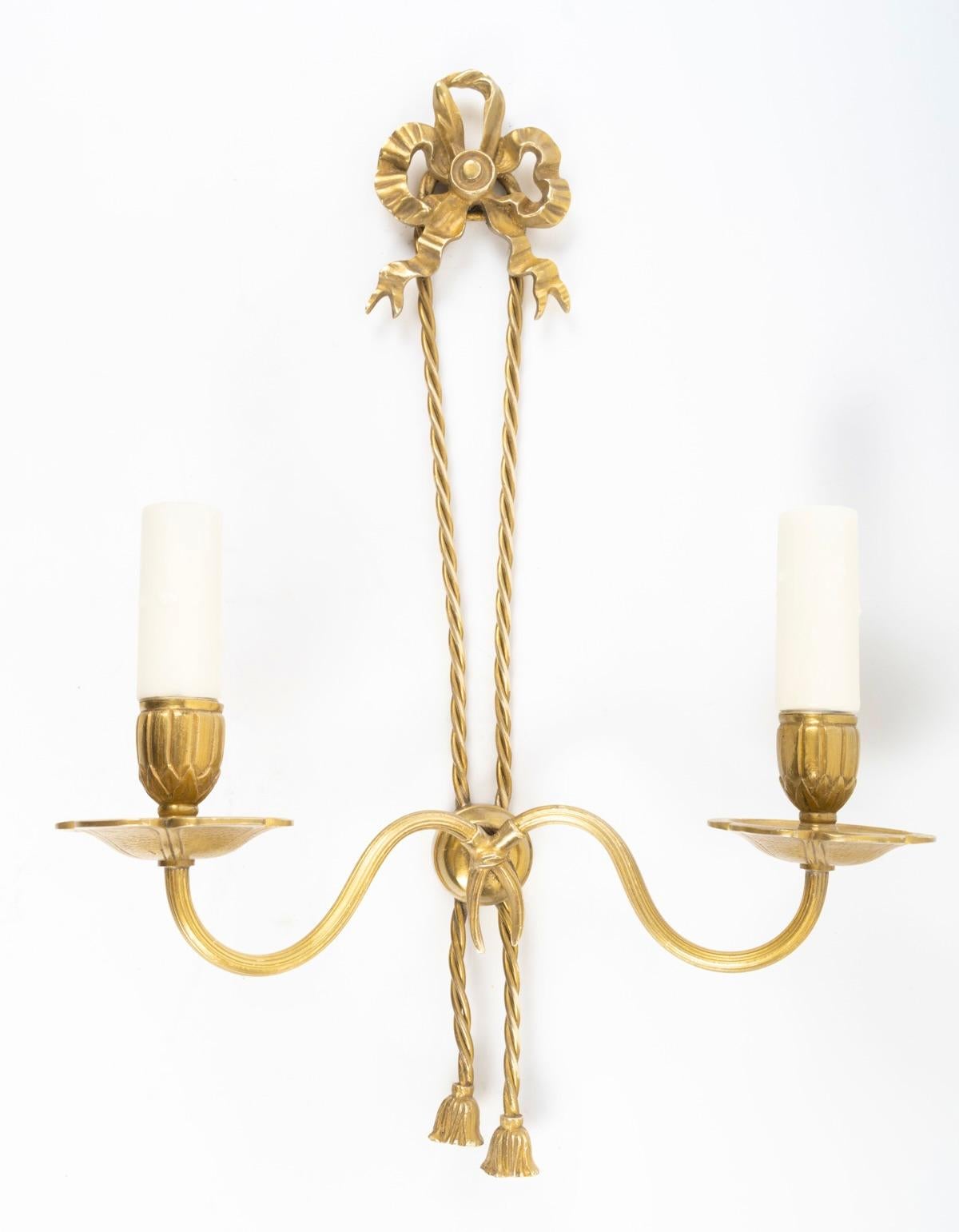 Sie besteht aus einer runden Wandhalterung, die auf beiden Seiten der Wandlampe zwei Leuchterarme trägt, die mit Bechern und Kerzen verziert sind, die auf Bobeches ruhen.
Ein hübsches Band, das eine Schleife im Louis XVI-Stil bildet, ist an der