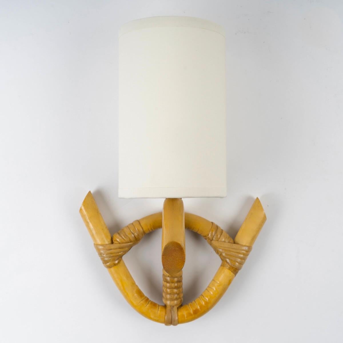 È composta da una staffa da parete in rattan su cui poggia un braccio luminoso formato da uno stelo di rattan curvo e situato nella parte anteriore dell'applique. Un paralume appoggiato sulla parte superiore dello stelo centrale in cotone bianco