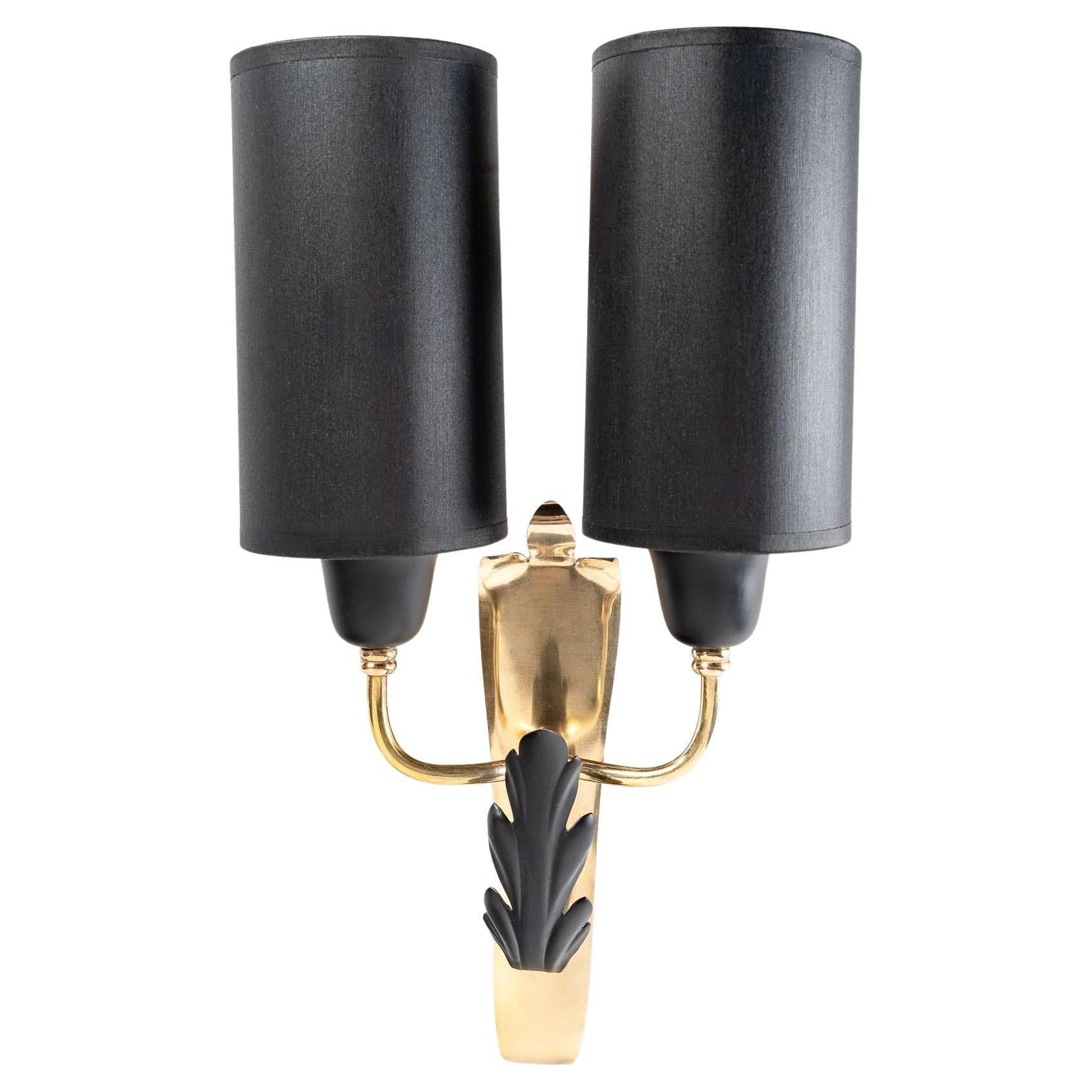 Composed of a wall base inspired by a gilded brass crest decorated on the lower part with a stylized oak leaf in blackened brass.
Just above, two small arms of light going up distributed on each side of the wall lamp are dressed with lampshades of