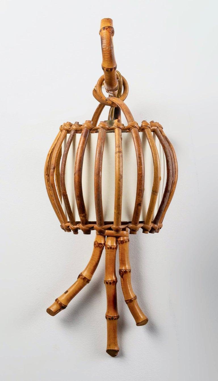 Composed of a wall support formed by a central stem underlined by two curved stems on both sides of the support, the whole in pretty bamboo stem.
 At the top of the central stem, a rattan loop holds a suspended lampshade formed on the outside by an
