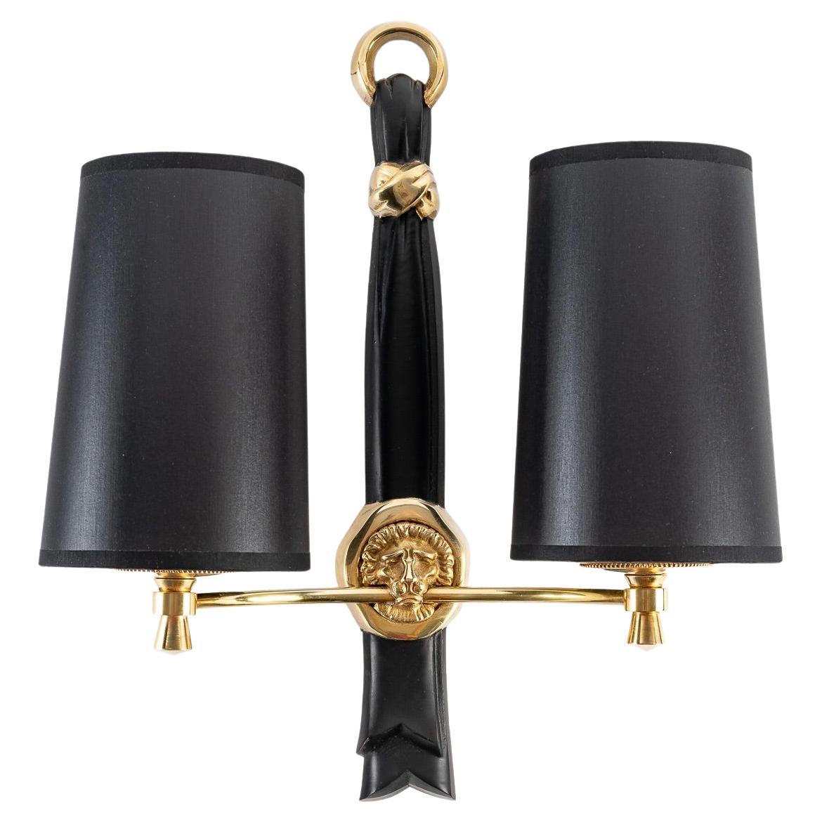 Pair of wall sconces with two lights in gilt bronze and black patina.
The central stem is composed of a draped ribbon with black patina passing through a gilded ring and held by a gilded bow. 
On the lower part, a gilded lion's head is decorated