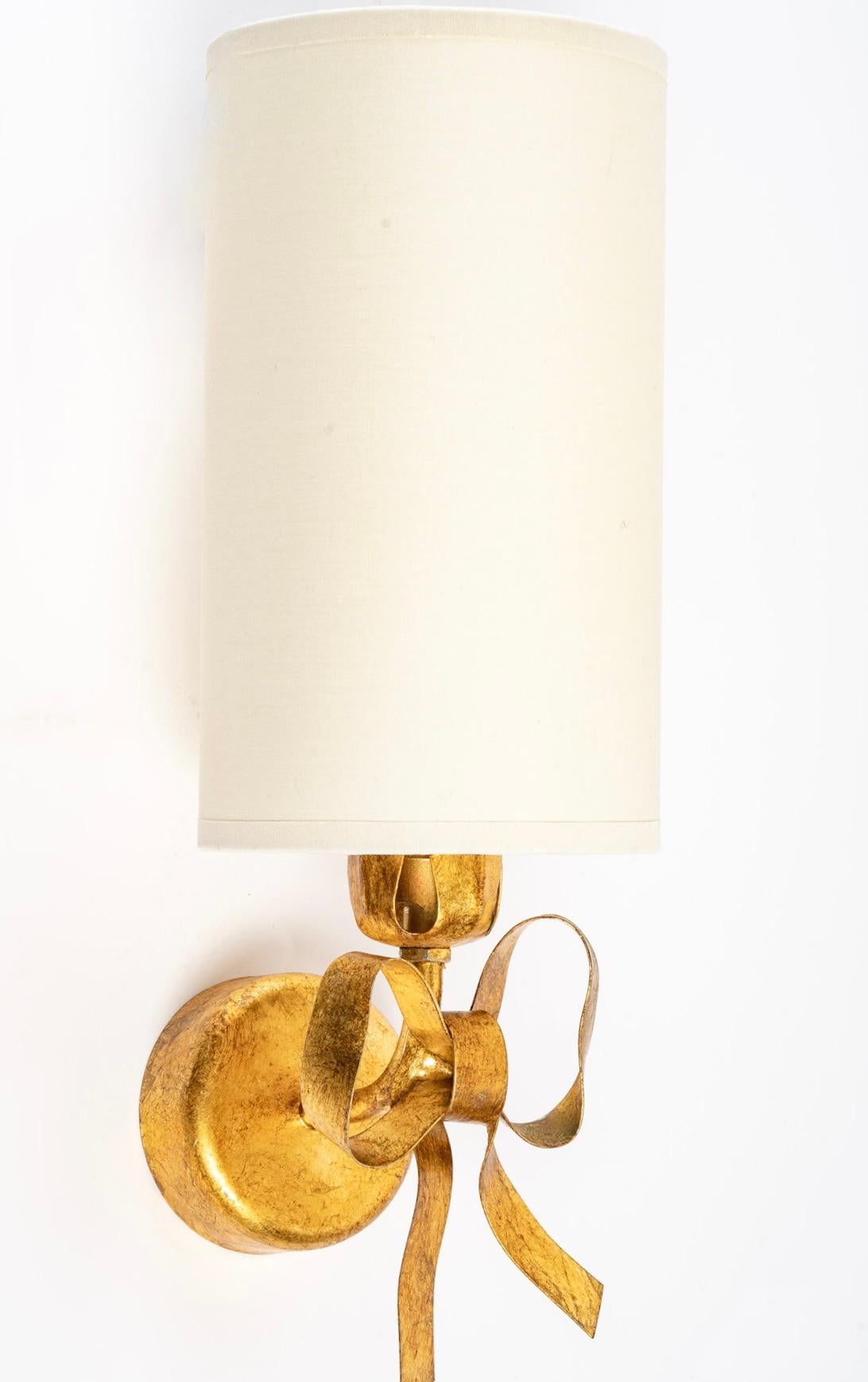 Composed of a round wall support on which is placed a pretty handmade knot, all in gilded metal.
The sconce is dressed with a lampshade in off-white cotton of cylindrical form underlined has its base of small leaves being used to hide the