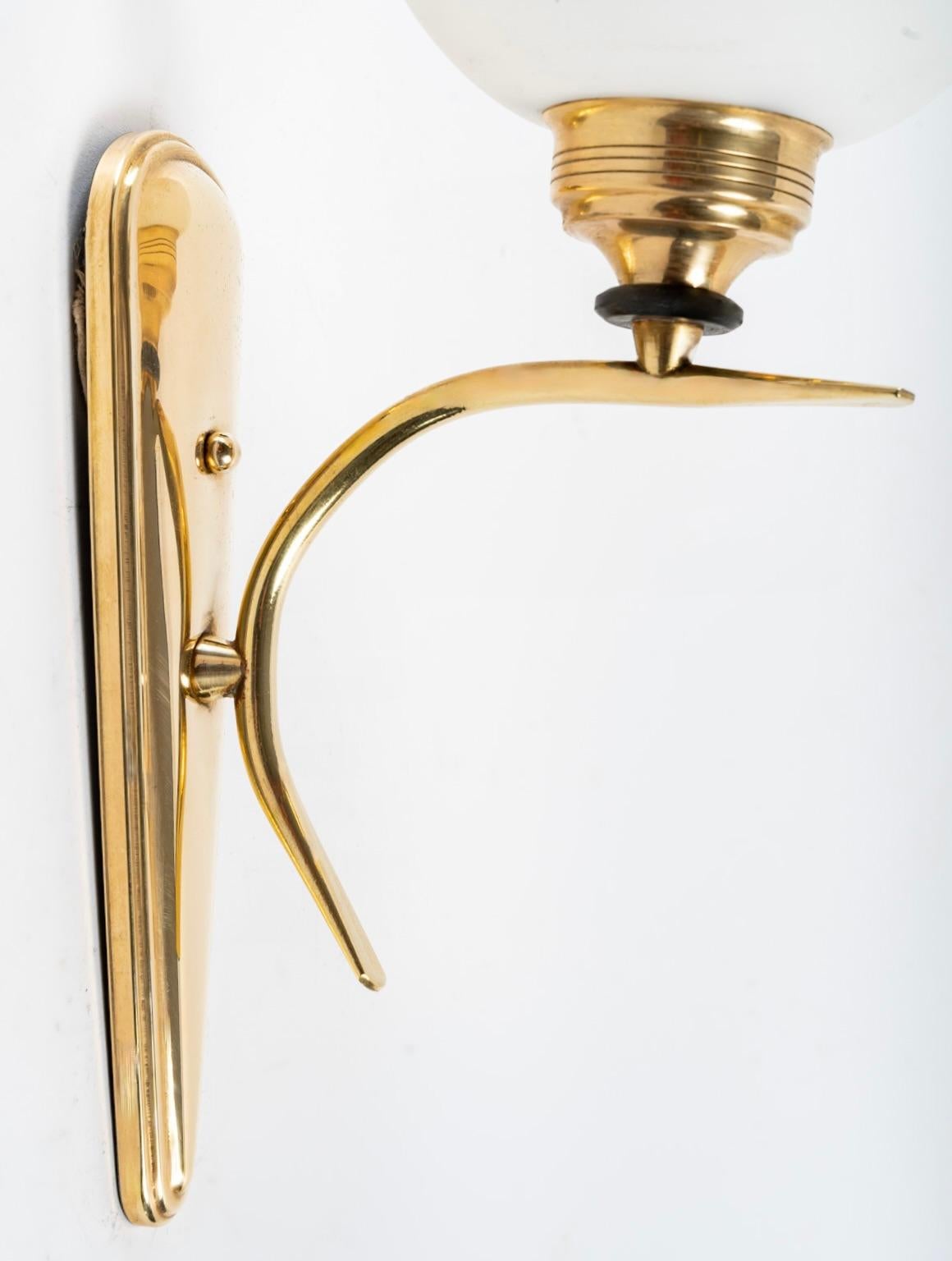 Composed of an oblong gilded brass wall base on which is placed a curved and tapered gilded brass light arm.
On the upper part of the arm is a round frosted opaline, it is placed on a gilded brass chalice-shaped support decorated with a black