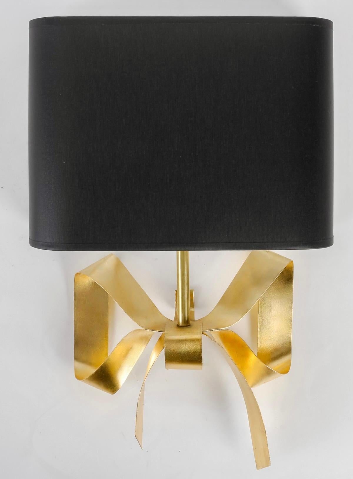Composed of a wall bracket forming a half-loop at the back of the sconce, on which rests a pretty handmade bow, all in gilded leaf metal.
The sconce is clad with a black cotton shade held in place by a gilded brass rod connected to the base at the