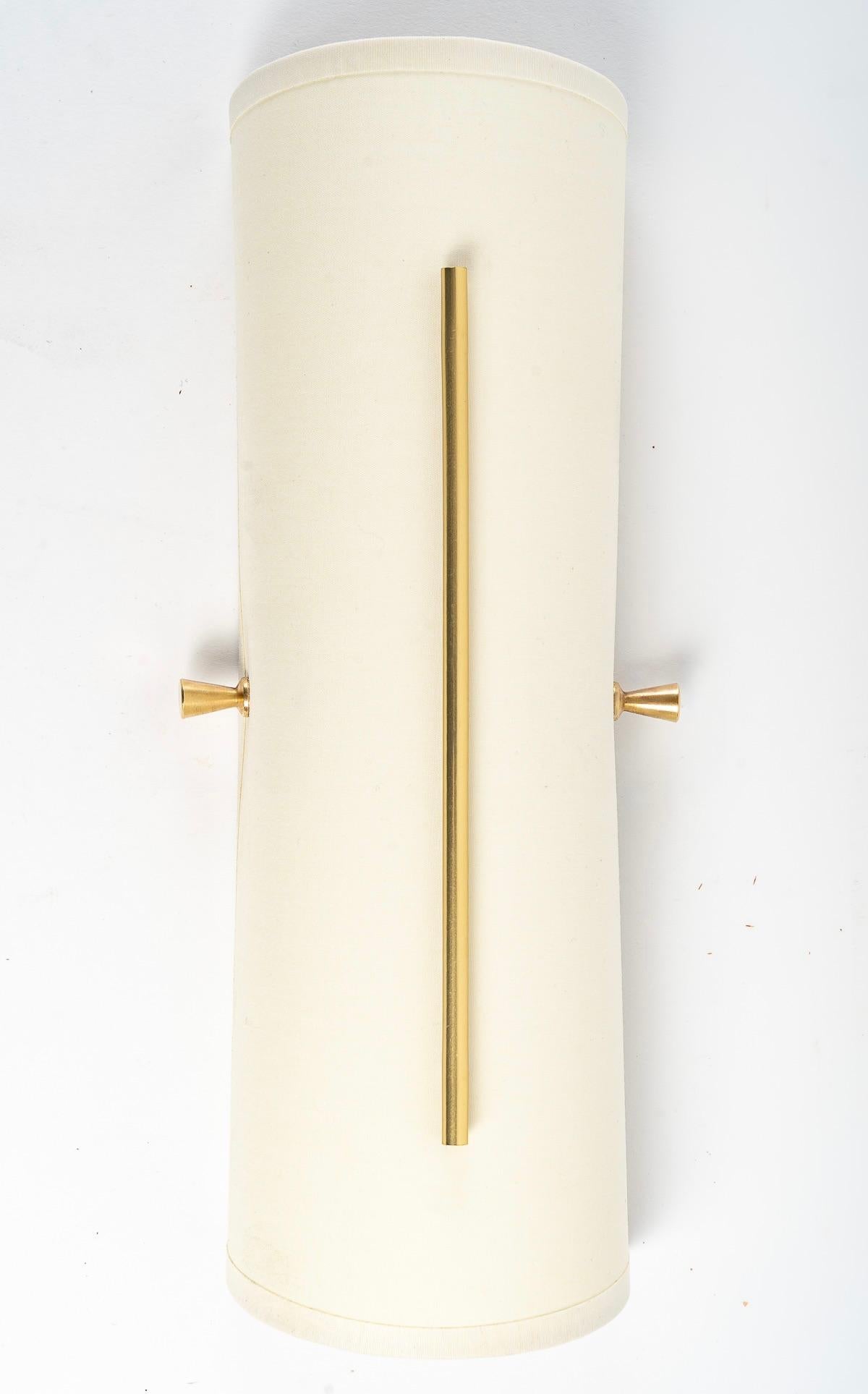 Original pair of sconces 
.
Composed of a half cylinder in off-white cotton positioned in height and maintained by two small spinning tops in gold brass positioned on each side of the sconce has put height. 
It is decorated on the front of the half
