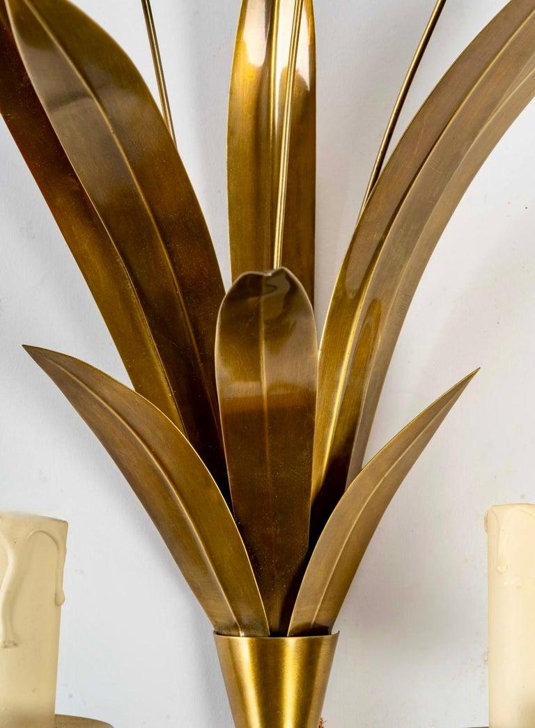 Each sconce is composed of 6 leaves of different sizes and decorated with 3 golden floral spikes forming a bouquet held in place by a cone.
On the lower part, two ascending light arms are dressed with candle lights.
The whole is in varnished brass