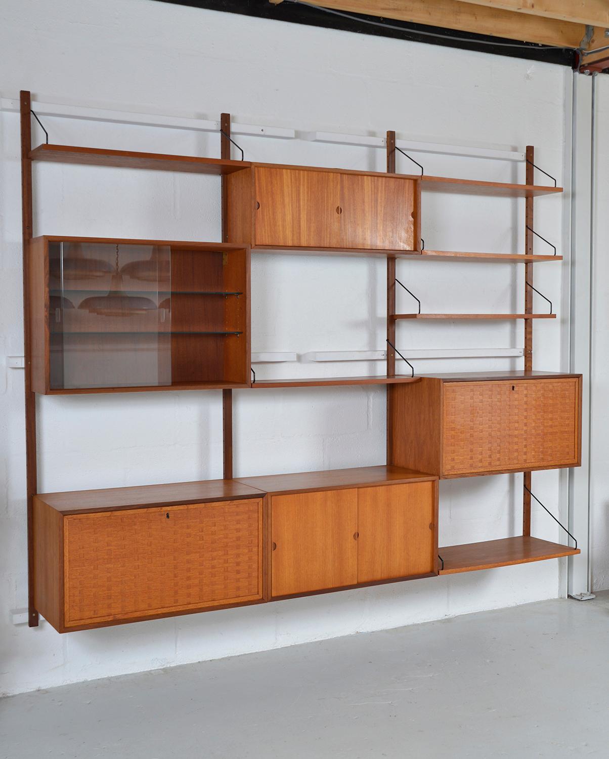 This highly versatile and functional “Royal System” was originally designed by Poul Cadovius in 1948. This three-bay teak shelving system offers a wide variety of storage and display options. 
The two attractive basket weave drop front cabinets are