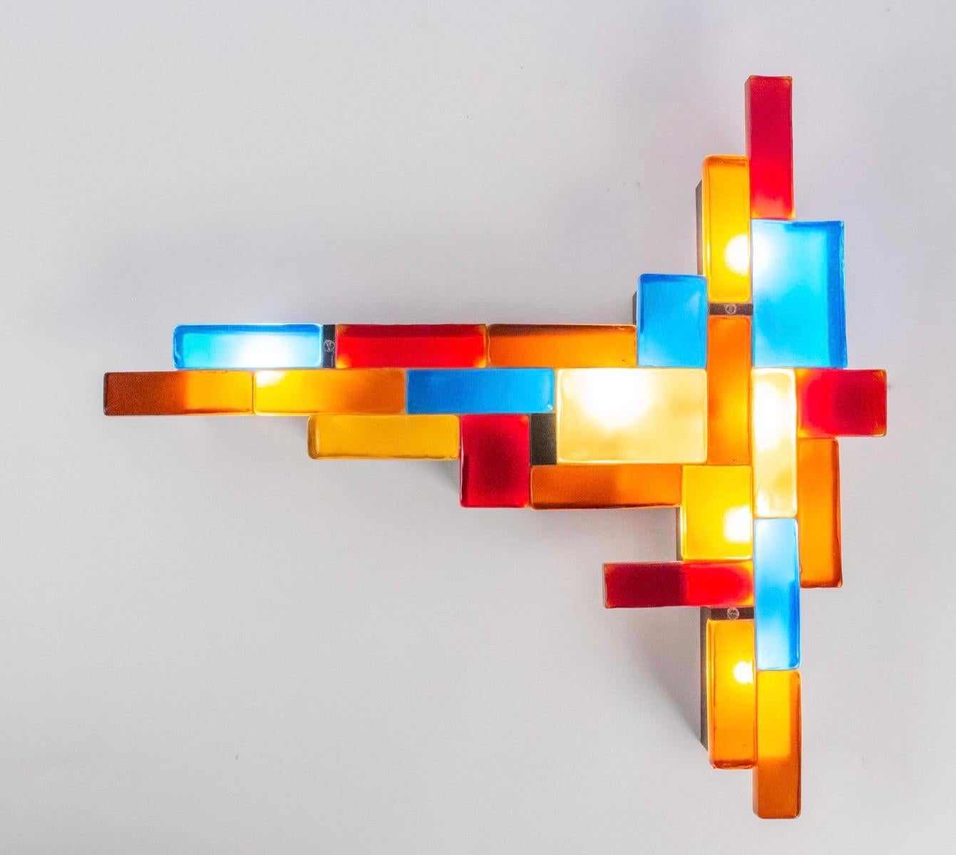 This rare and large sconce is composed of different pieces of tinted glass slabs. The colors range from blue, yellow, orange and red. All the stained glass pieces are mounted on a blackened wrought iron frame. 
The 7 bulbs provide a soft and