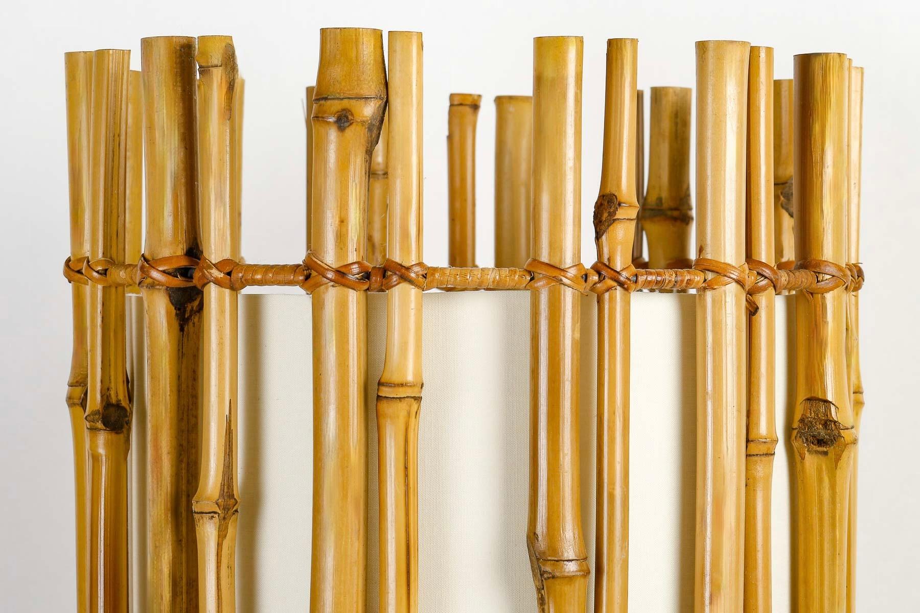 Composed of a cylinder of vertically positioned bamboo stems held together by 3 rattan-wire-clad circles at 3 different heights.
The bamboo cylinder is lined with an off-white lampshade placed inside it, highlighting the rattan rods.

1 light arm.