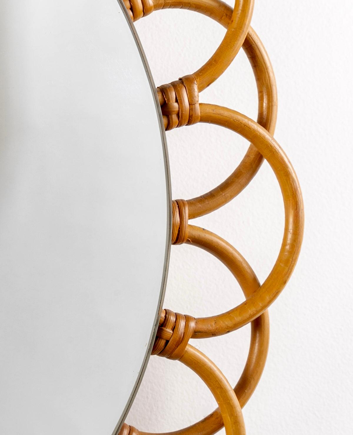 Composed of a circular mirror underlined on the perimeter of rattan stems forming half-circles around the mirror and decorating the mirror nicely.
On the upper part a rattan chain formed by small intertwined loops is joined on the upper part by a