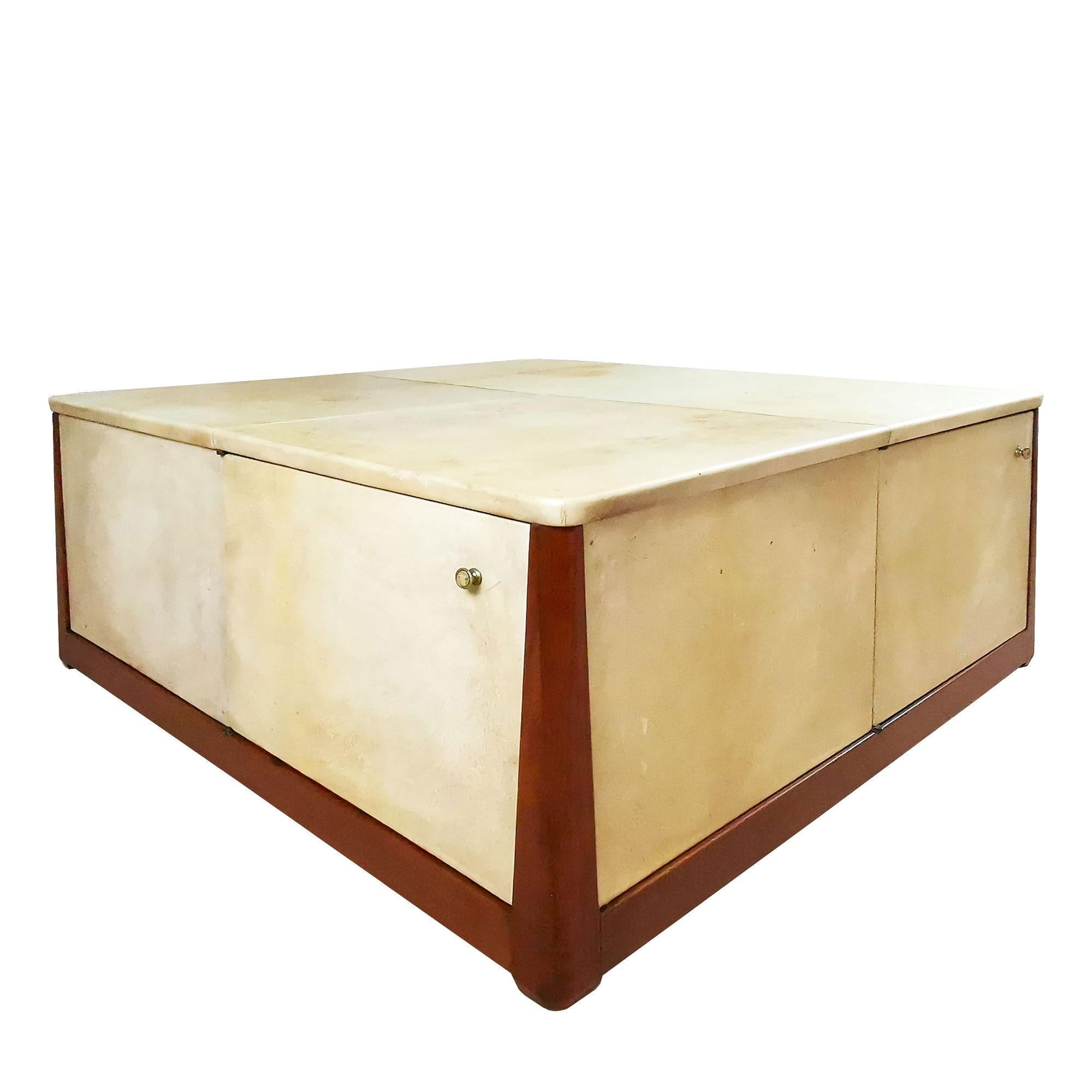 Large square coffee table, solid mahogany structure and thick plywood, completely covered with parchment (original patina) except the stands, three doors on the sides and one flap door on top for storage. Polished brass hardware. 
Design: Pere Cosp