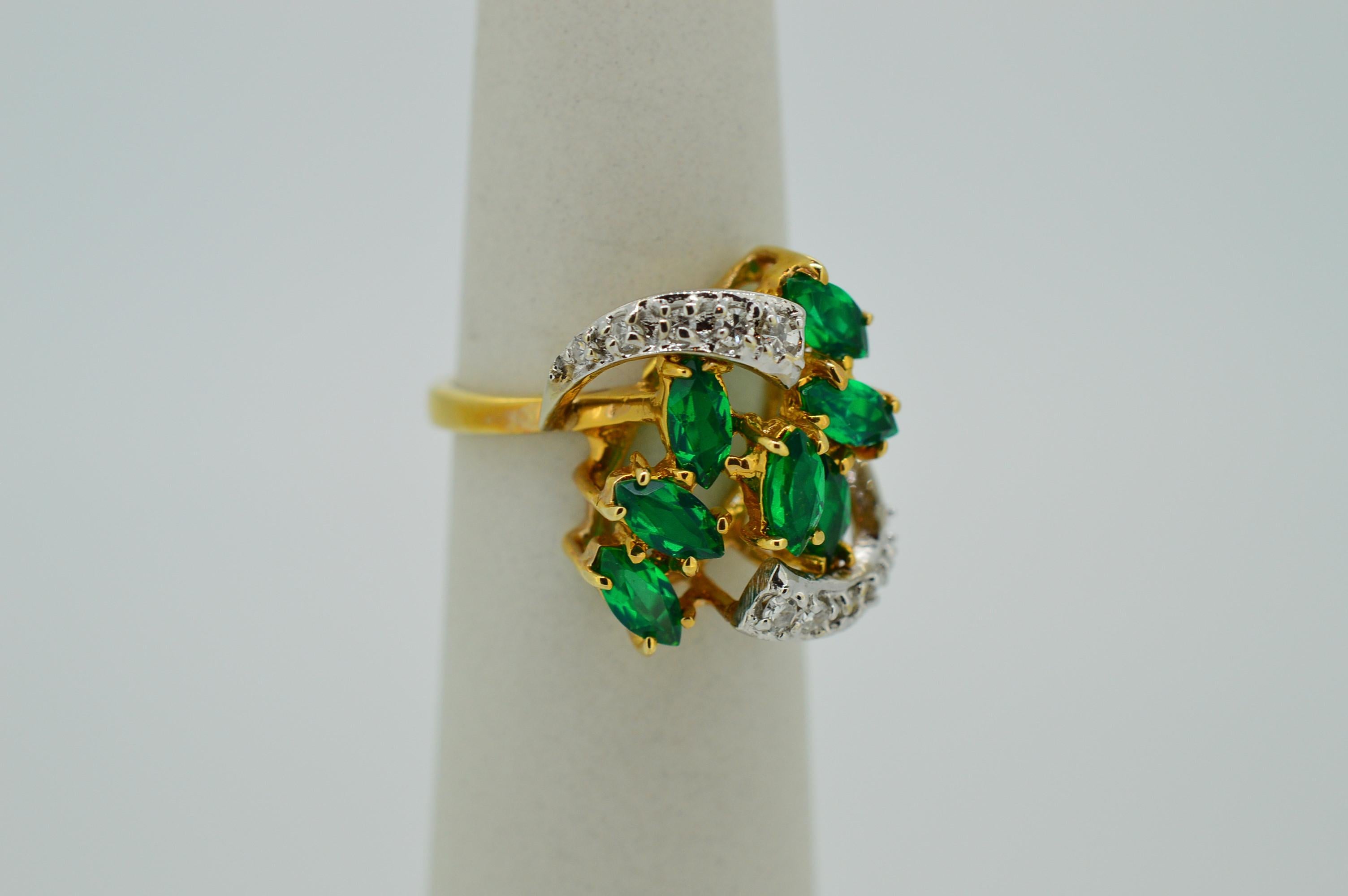 Two diamond enhanced flares surround seven vibrant green floating marquis-cut beryl doublets to create this whimsical 1960's style fourteen karat 
(14k) yellow gold cocktail ring. Designed with a cluster of seven .20 carats marque-cut beryl doublets