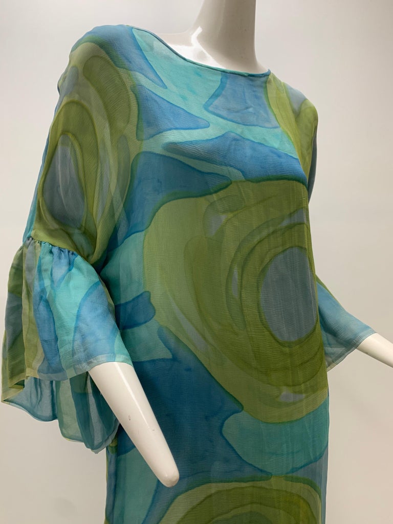 A late 1960s silk chiffon shift dress in aqua and green hand-painted abstract floral designs with asymmetrical ruffles at hem and cuffs. Lined. No closures, slips over the head. 
