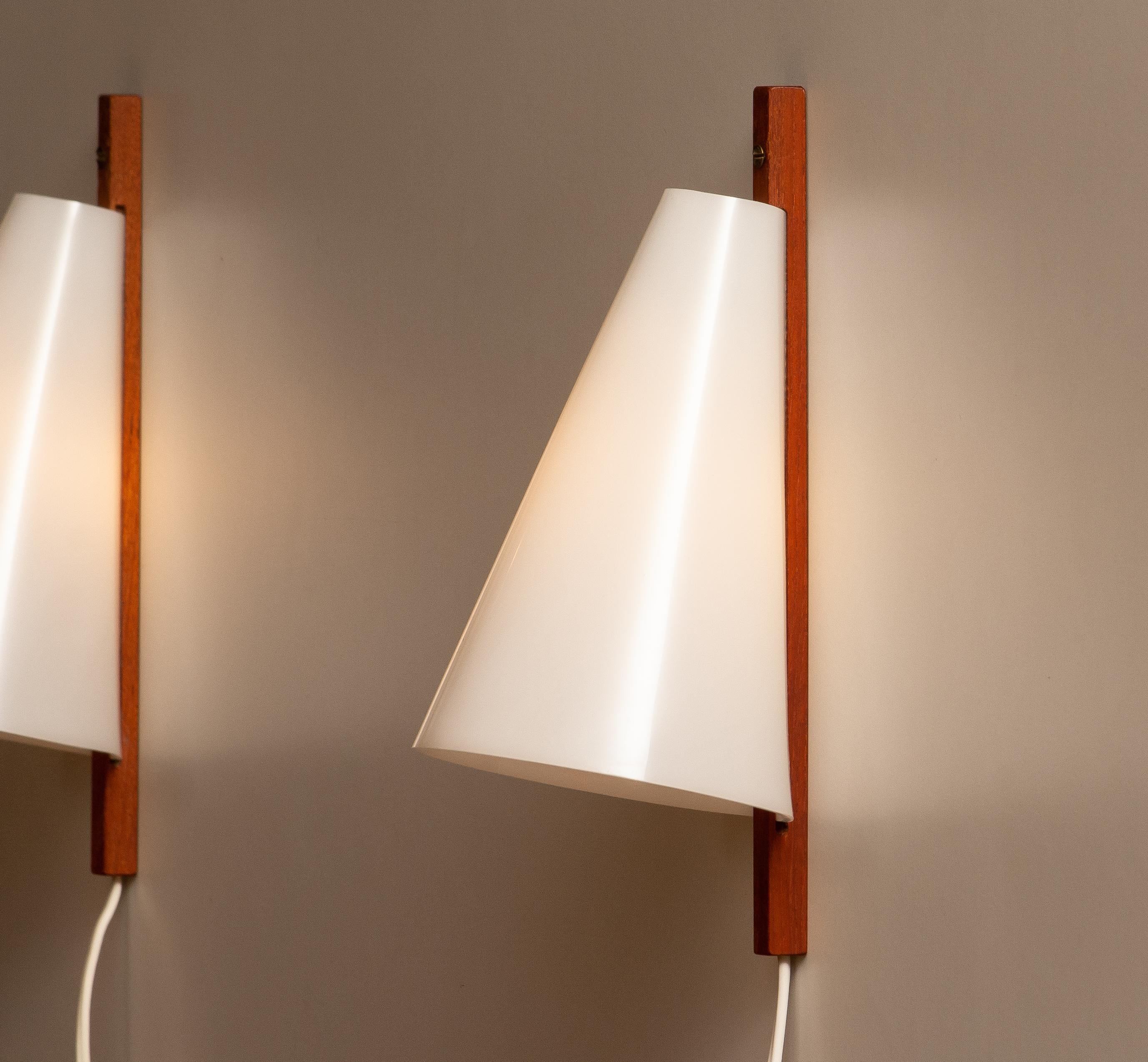 Original 1960's wall lights / scones designed by Uno & Östen Kristiansson for LUXUS, Vittsjö in Sweden. The wall lights are made of acryl plastic shade in white and a wall fixation in teak. Technically 100% and both wall lights have a screw fitting