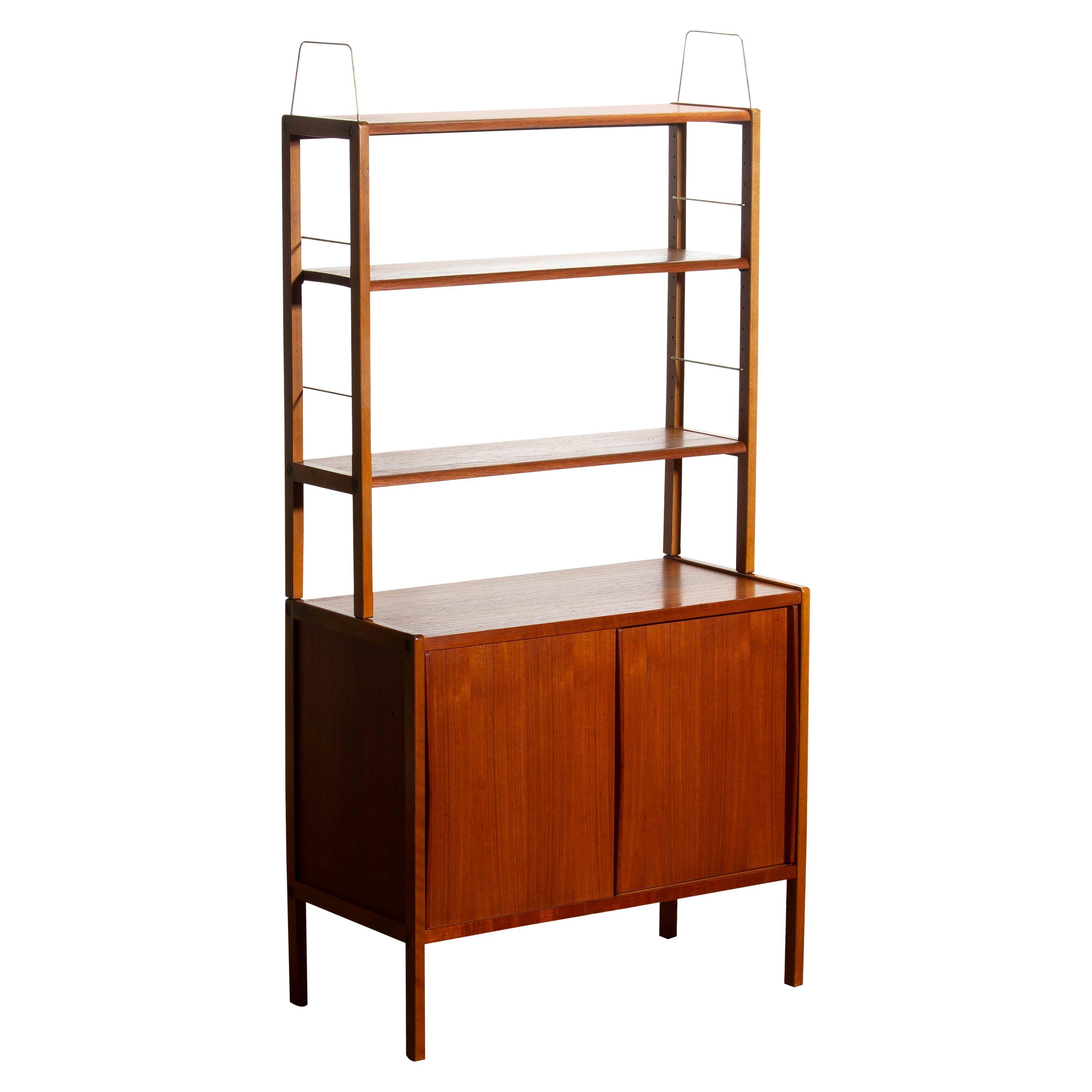 Beautiful and elegant teak bookcase cabinet with brass detail and two sliding doors by Bertil Fridhagen for Bodafors, Sweden, 1960s.

The lower part of the cabinet has two sliding doors and inside the original shelf with burned logo 