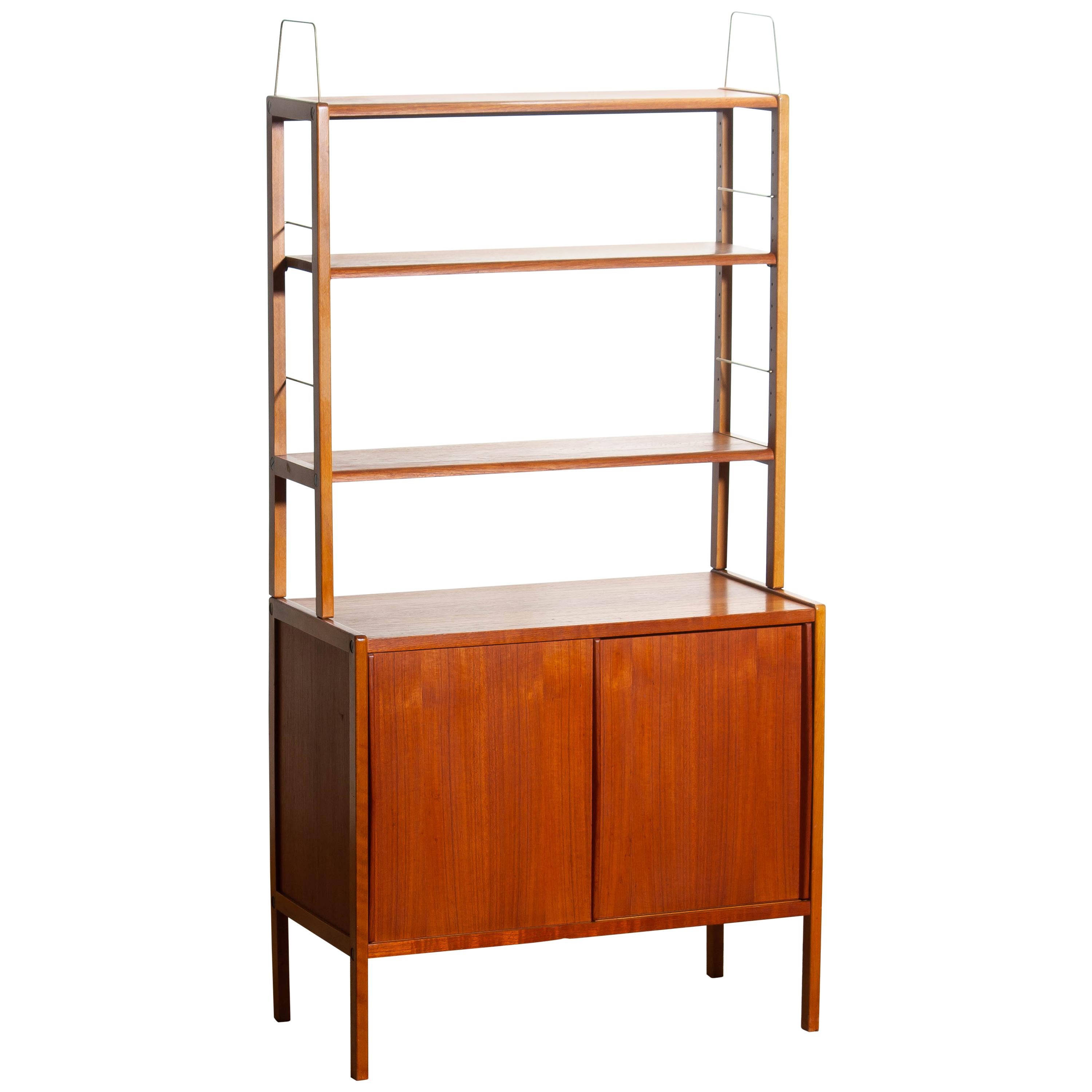 Beautiful and elegant teak bookcase cabinet with brass detail and two sliding doors by Bertil Fridhagen for Bodafors, Sweden, 1960s.

The lower part of the cabinet has two sliding doors and inside the original shelf with burned logo 