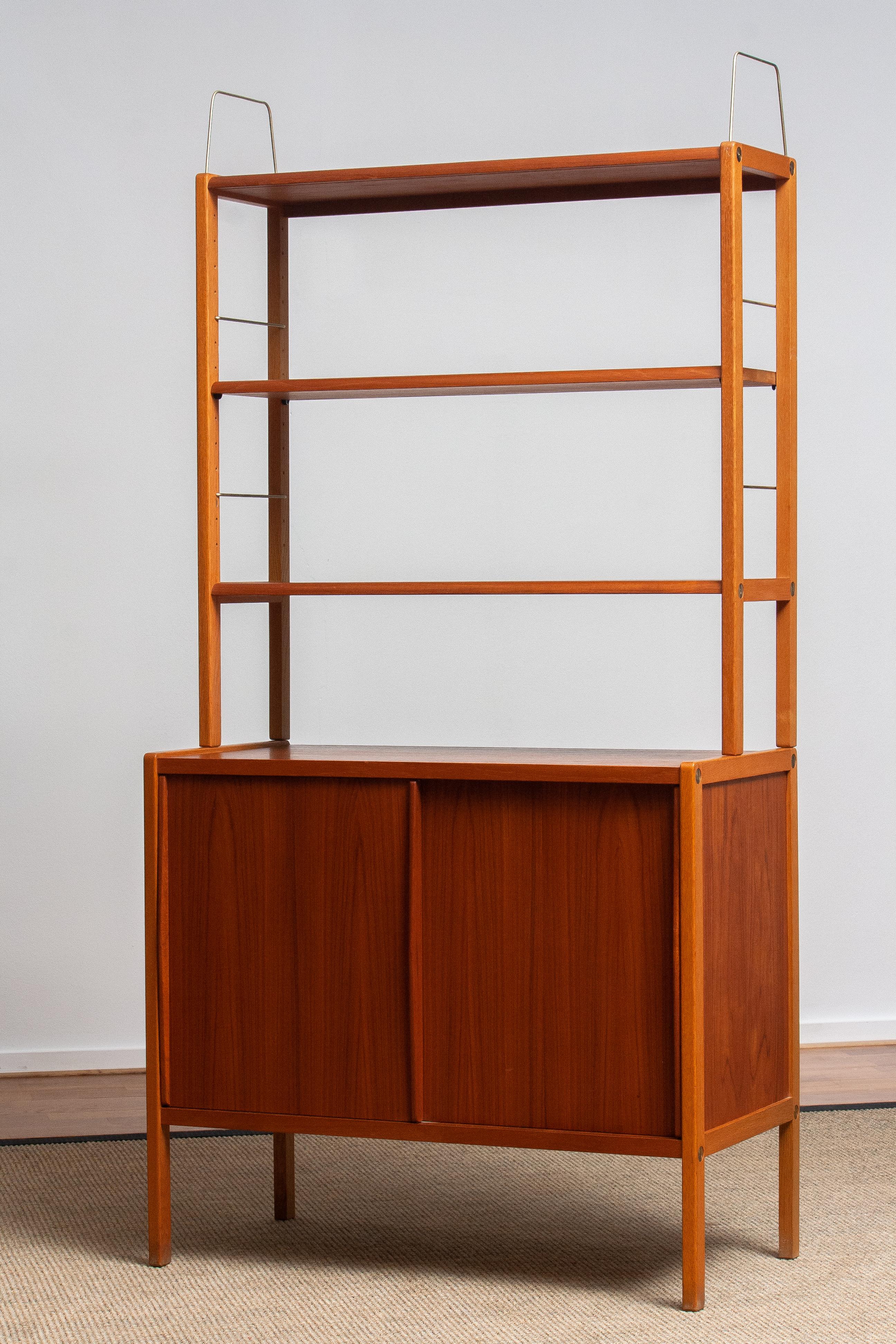 Beautiful and elegant teak bookcase cabinet with brass details by Bertil Fridhagen for Bodafors, Sweden, 1960s.

The lower part of the cabinet has two sliding doors and inside the original shelf with logo 