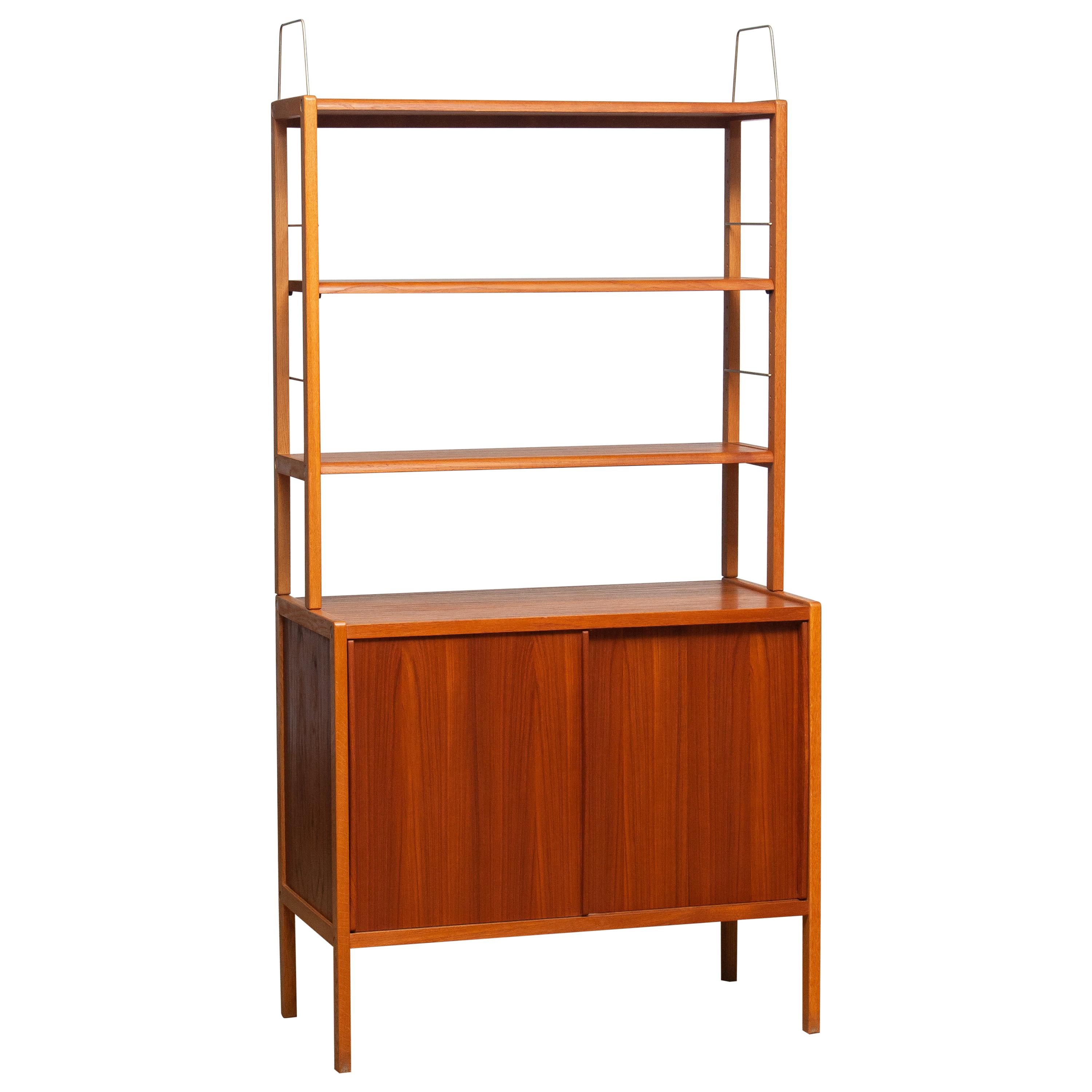 Beautiful and elegant teak bookcase cabinet with brass details by Bertil Fridhagen for Bodafors, Sweden, 1960s.

The lower part of the cabinet has two sliding doors and inside the original shelf with logo 