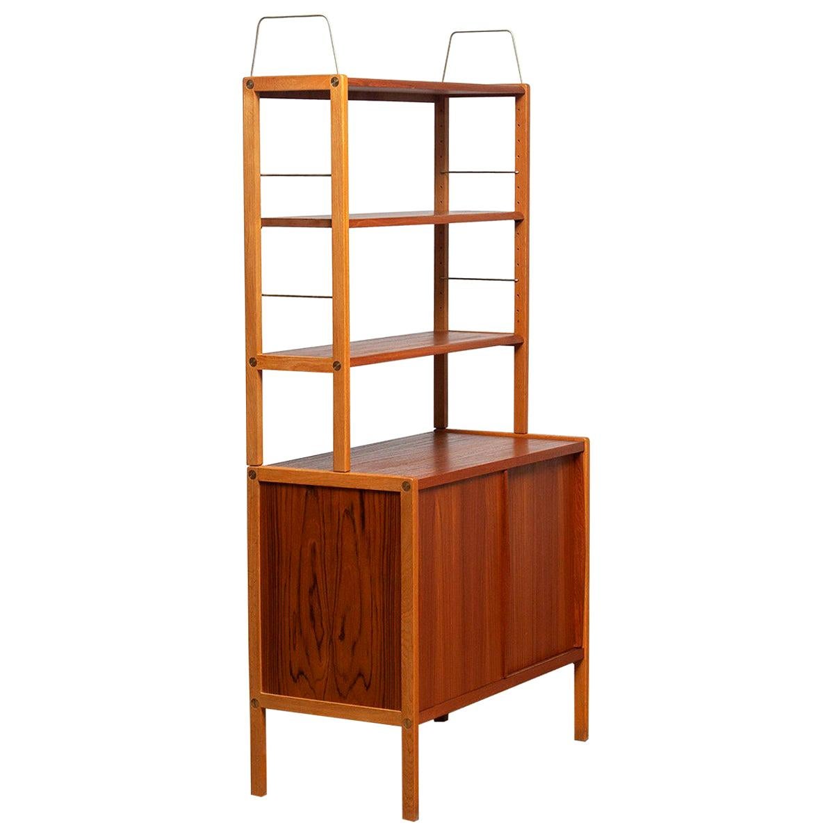 Beautiful and elegant teak bookcase cabinet with brass details by Bertil Fridhagen for Bodafors, Sweden, 1960s.

The lower part of the cabinet has two sliding doors and inside the original shelf with logo 