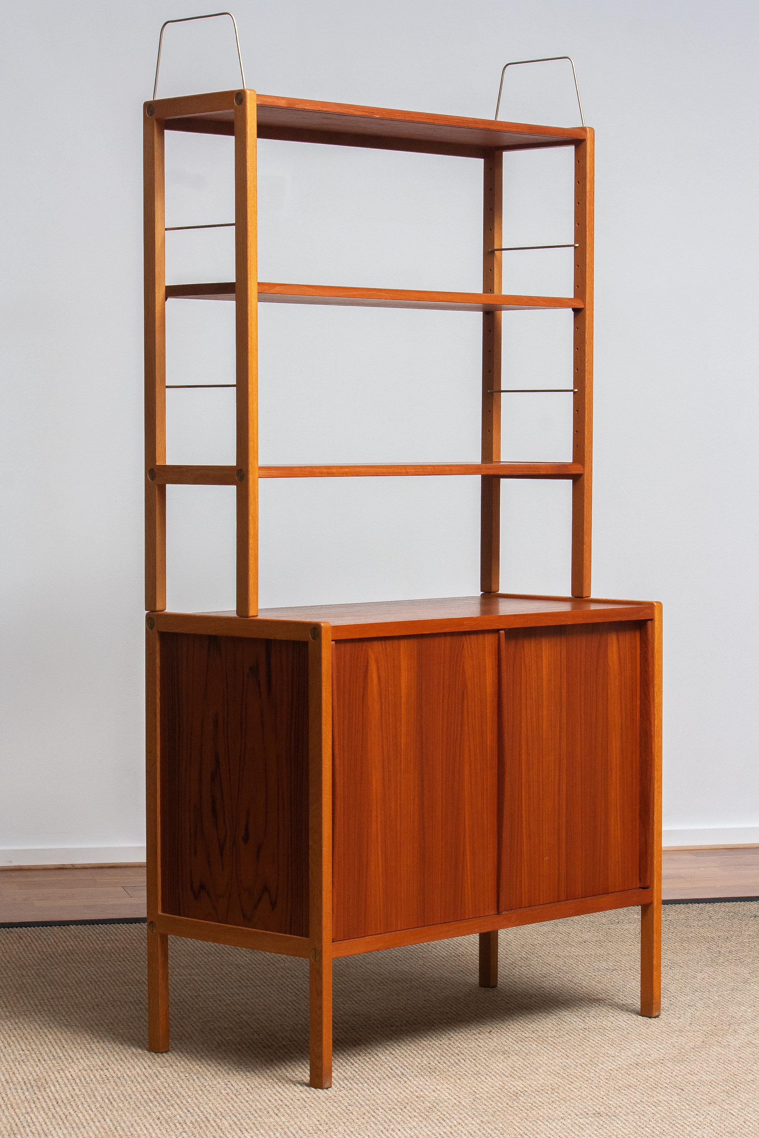 Beautiful and elegant teak bookcase cabinet with brass details by Bertil Fridhagen for Bodafors, Sweden, 1960s.

The lower part of the cabinet has two sliding doors and inside the original shelf with logo 