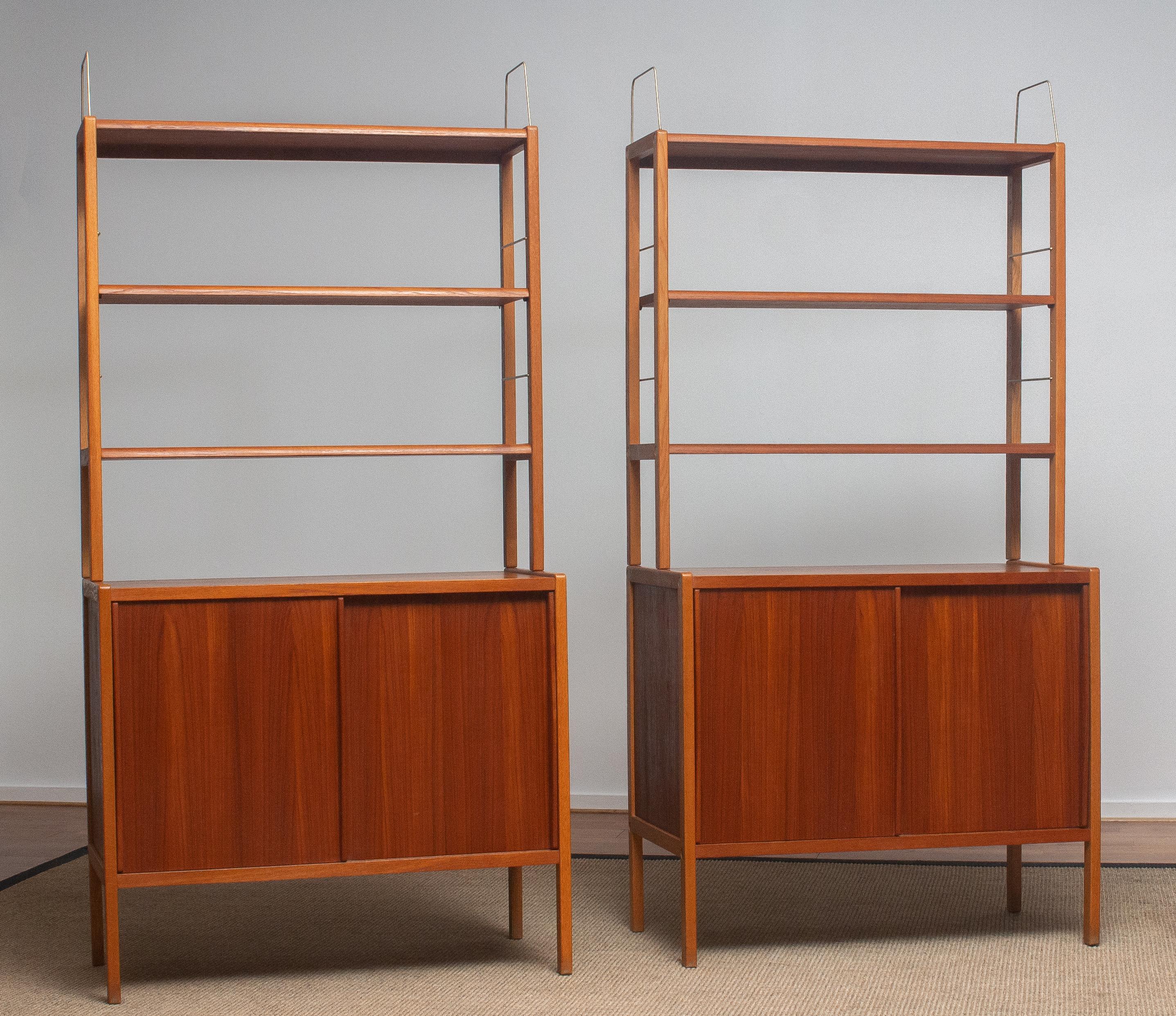 Beautiful and elegant set of two teak bookcases / cabinets with brass details and two sliding doors by Bertil Fridhagen for Bodafors, Sweden, 1960s.

Both lower parts of the cabinets have two sliding doors and inside the original shelfs with logo