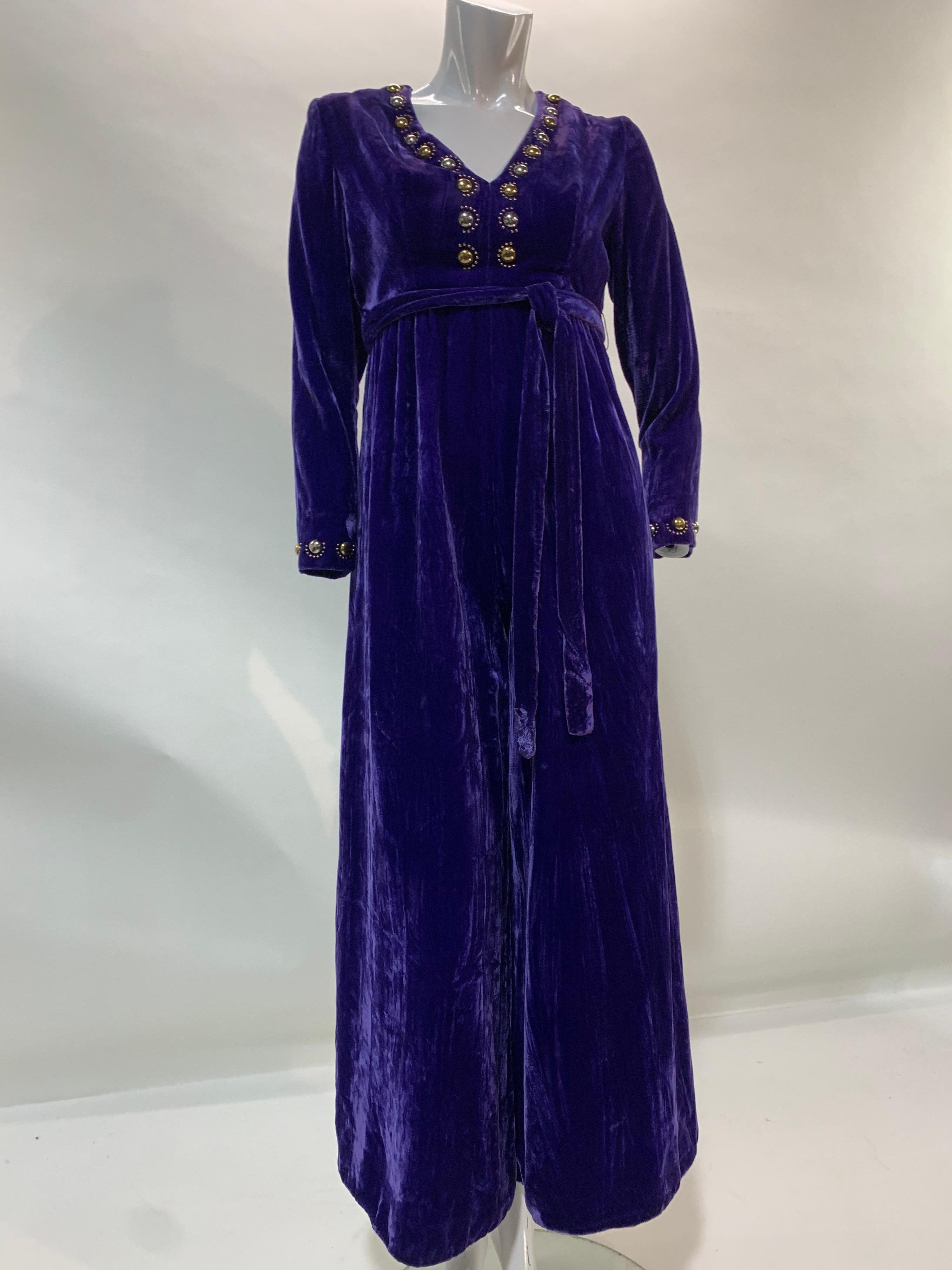 A 1960s Futura Couture vivid purple rayon velvet jumpsuit with gold and silver toned half sphere stud embellishments at neckline and cuffs. Wide flared leg and back zipper. Original belt included. Back zipper. Fully lined. Size 6