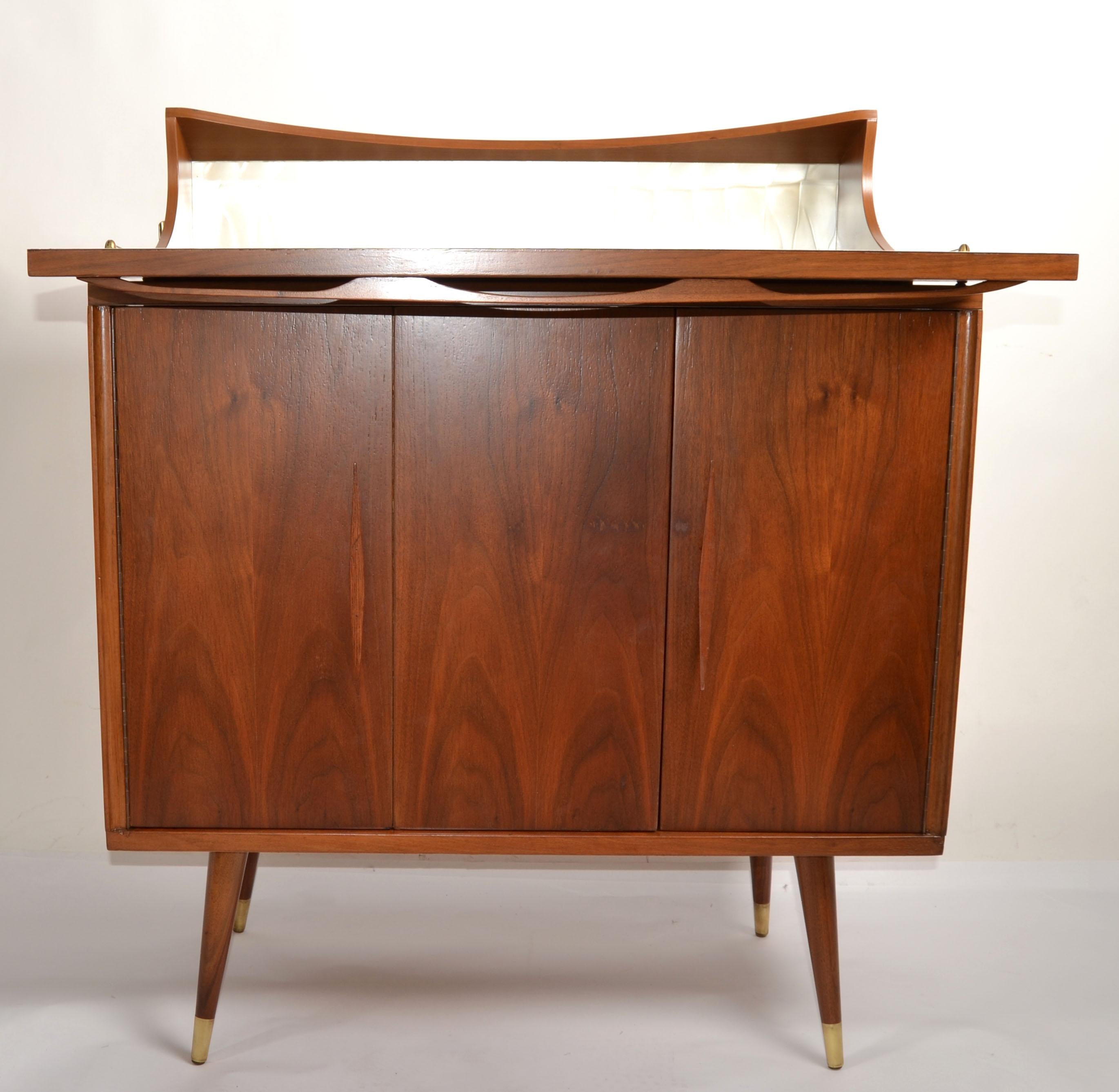 Charming Mid-Century Modern American Versatile Walnut Dry Bar, Server or Drinks Cabinet with pull up, flip up Formica top as a mixing Platform with Bottle and Glass shaped cutouts.
The center reveals enough storage compartment, behind 2 swing doors.