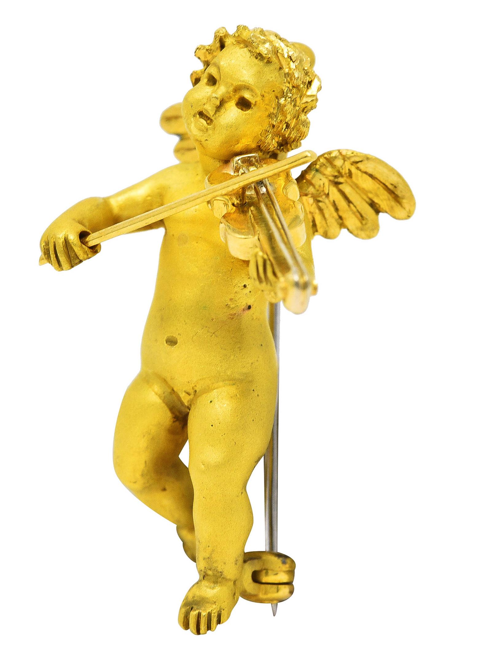 Pendant brooch is designed as a highly rendered winged cherub playing the violin. With texturous hair, engraved feathered wings, and high polished violin. Completed by jump ring and hinged pin stem with locking closure. Stamped 750 for 18 karat
