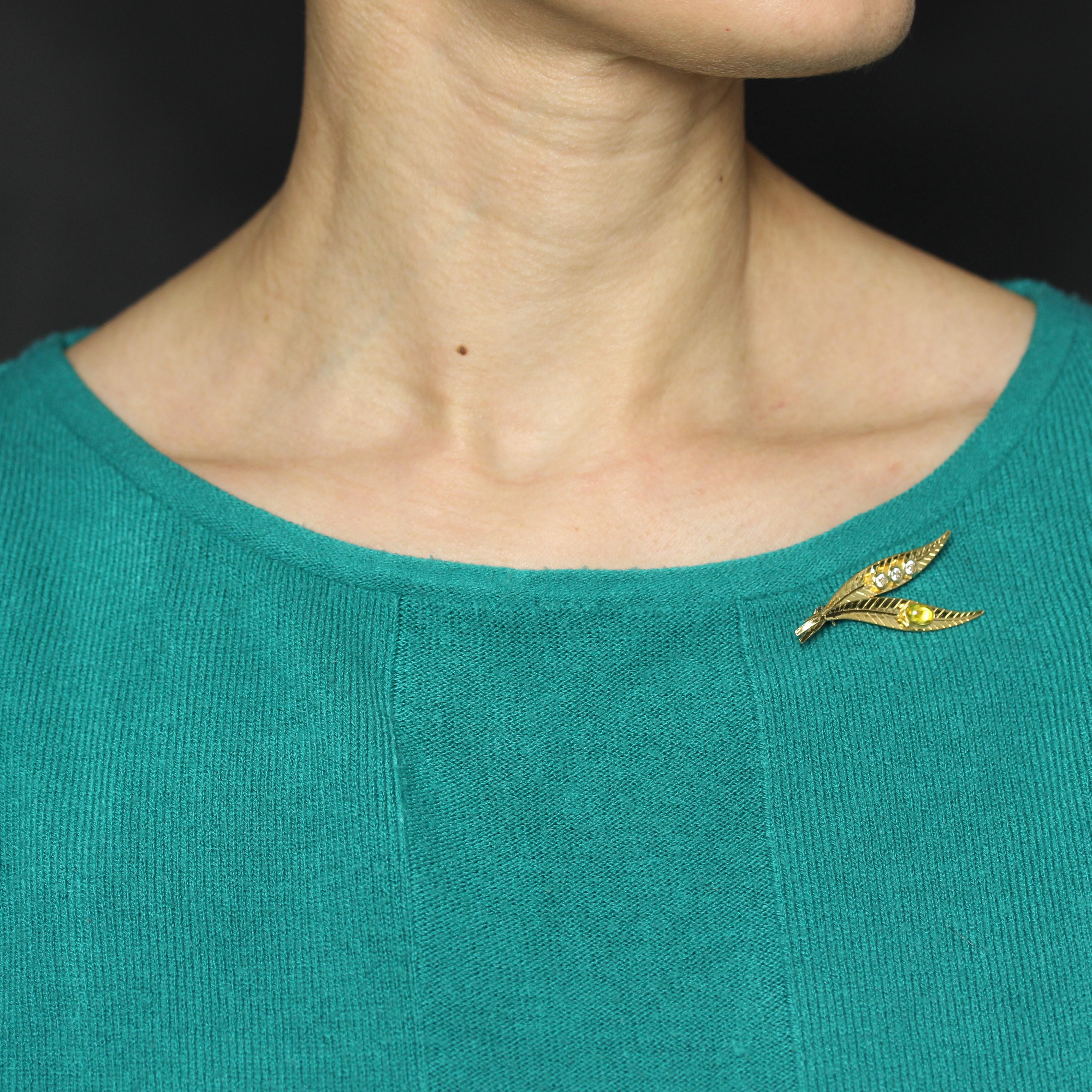 Brooch in 18 karat yellow gold.
This vintage brooch features two leaf motifs, one adorned with a cabochon yellow stone in a closed setting, the other with three white stones also in a closed setting. The fastening system is a safety pin.
Length :