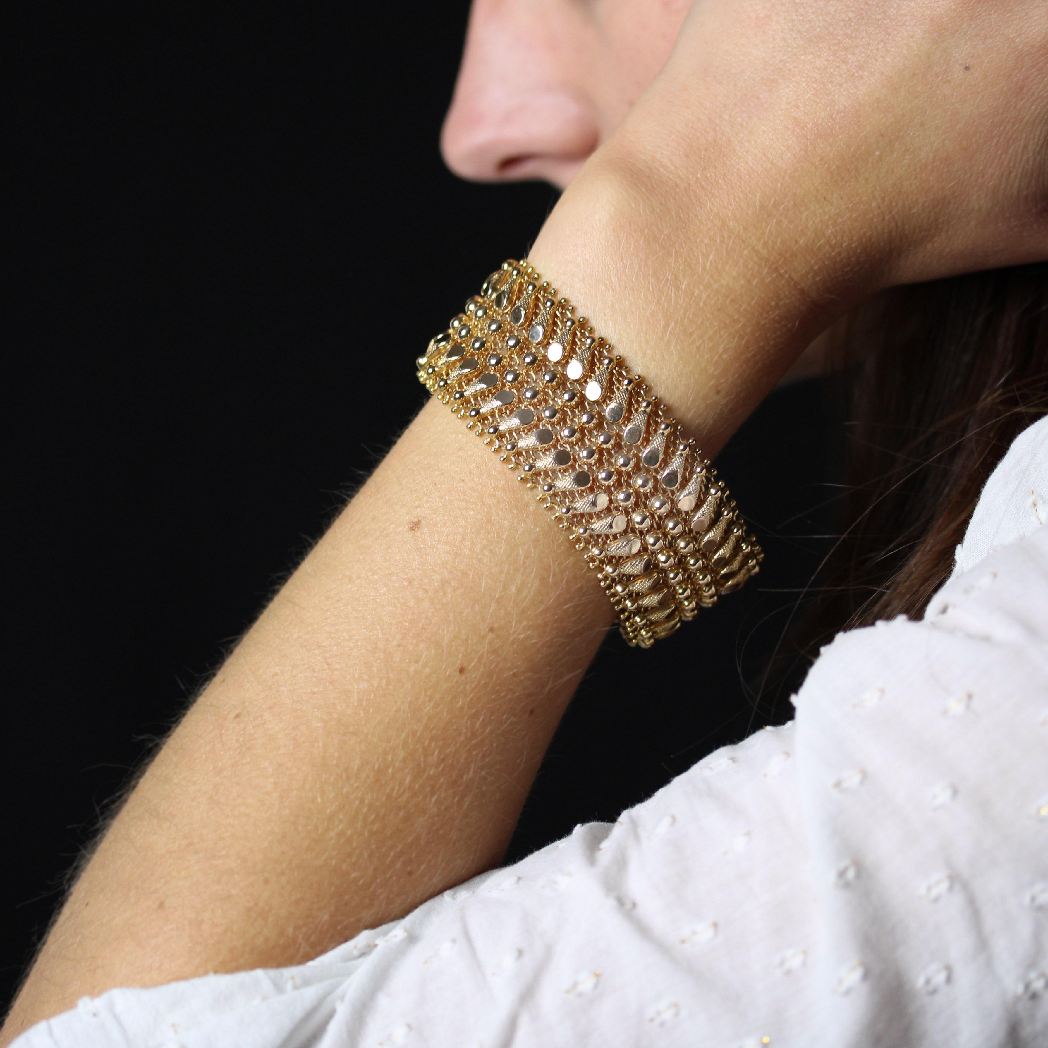 Bracelet en or jaune 18 carats, poinçon hibou.
Ce bracelet très souple en or jaune ancien est composé de fils d'or entrelacés comme un tissu. Le sommet est décoré de demi-sphères d'or et de petits motifs tels que des cônes ciselés. Le fermoir est un