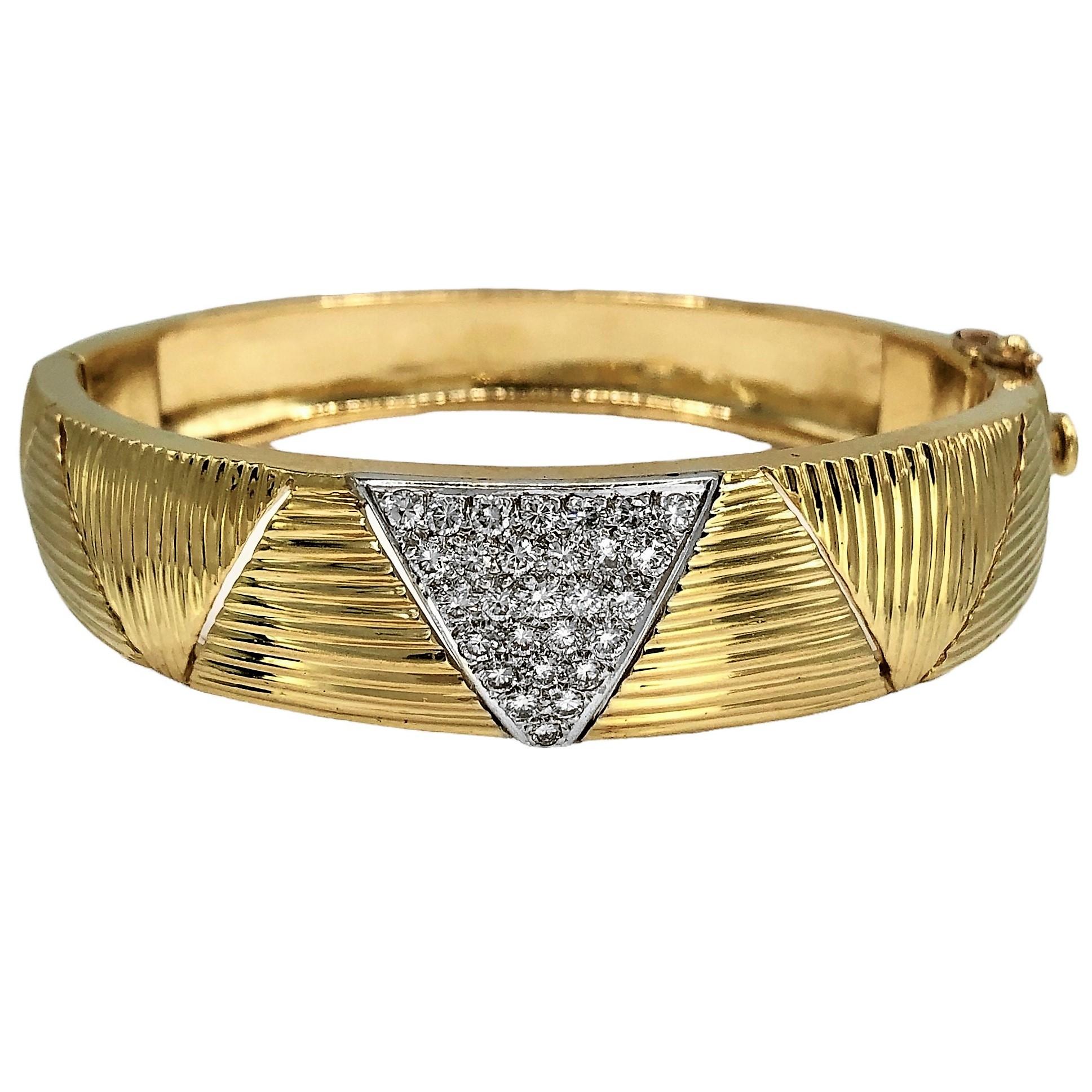 This beautifully executed 18k gold bangle bracelet graduates at the center from a width of almost 5/8 inches in width to 3/8 inches at the rear. One prominent pave triangle motif at the front is set with twenty eight brilliant cut diamonds with a
