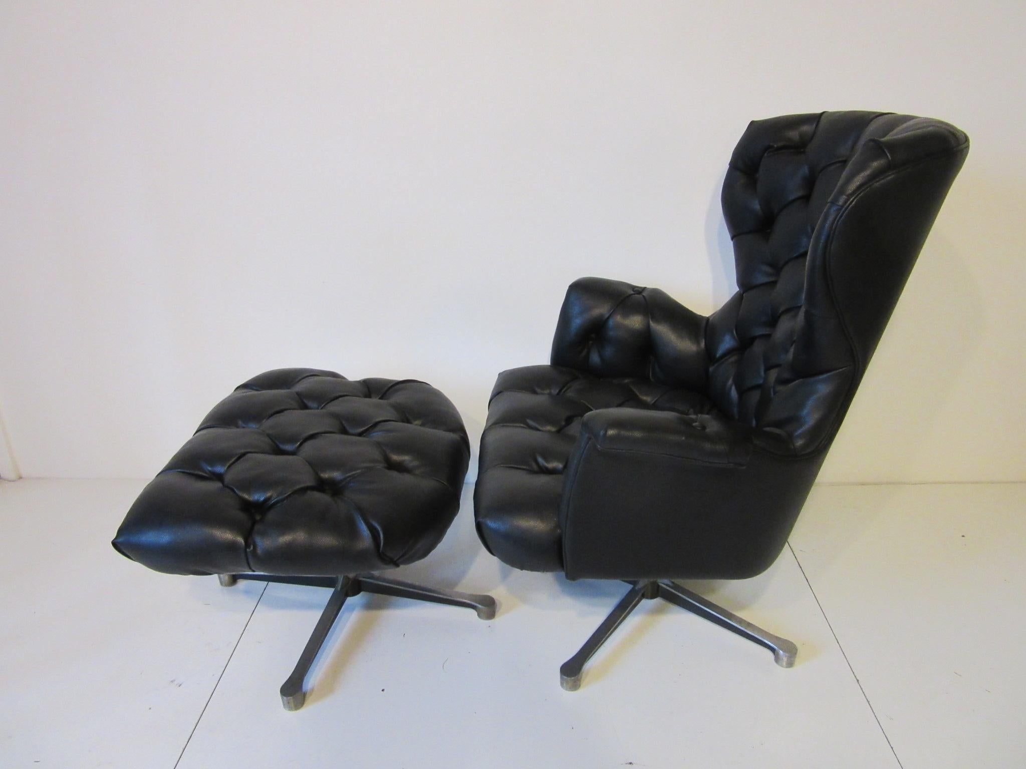 A lounge chair and matching ottoman in a very tight pebbled heavy black leatherette with tufted upholstery and cast aluminum swivelling bases. The chair itself has a spring to the bottom of the seat for rocking comfort, ottoman measurement is 26.25