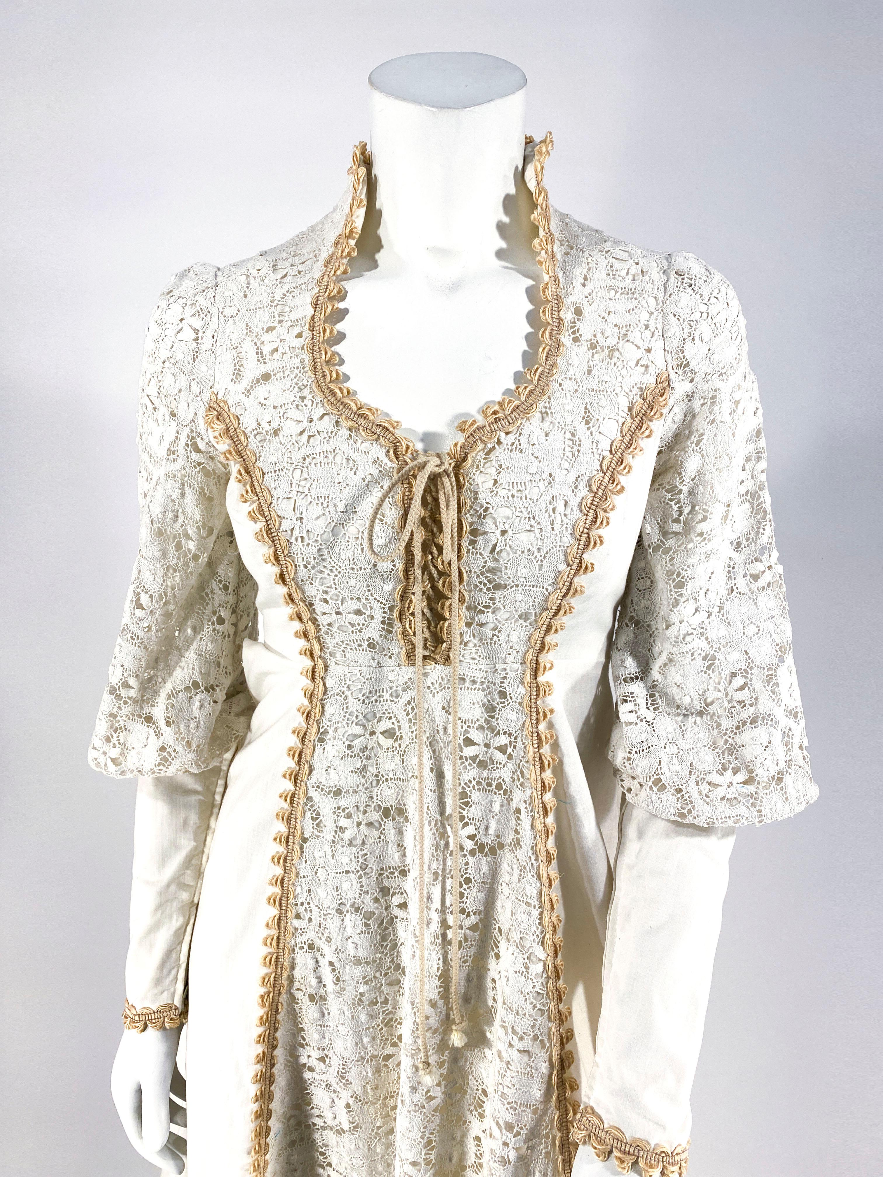 Late 1960s to early 1970s Gunne Sax cream prairie/cottage dress featuring crochet lace paneling alone the face of the dress and sleeves. The high neckline features a lace-up bust and is decorated with specialty hemp brick-a-brac trim. The bishop