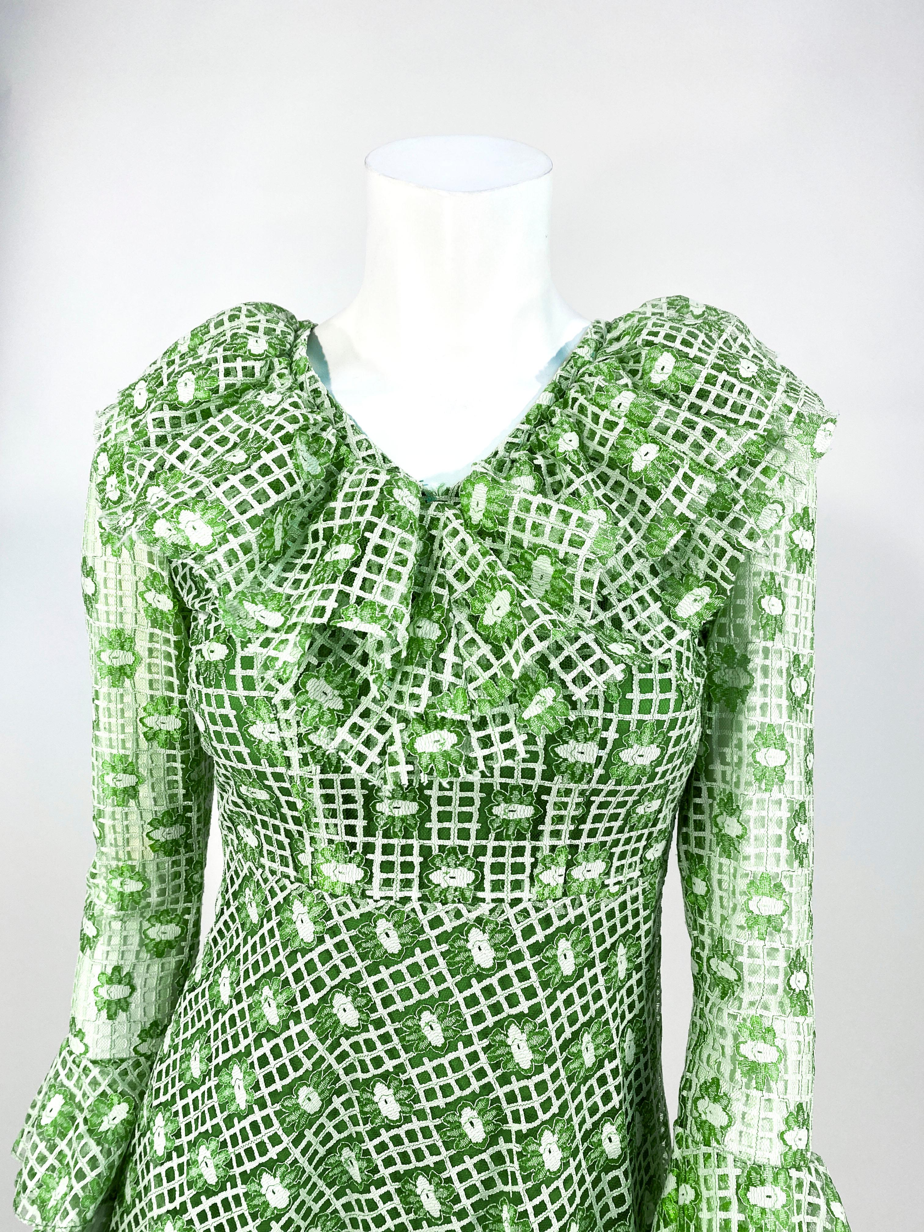 Petit Late 1960s to early 1970s green machine lace and mesh dress featuring a plaid and flower pattern. The body of the dress is fully lined and the sleeves are sheer. The neckline and cuffs are adorned with wide gathered ruffles. The skirt is