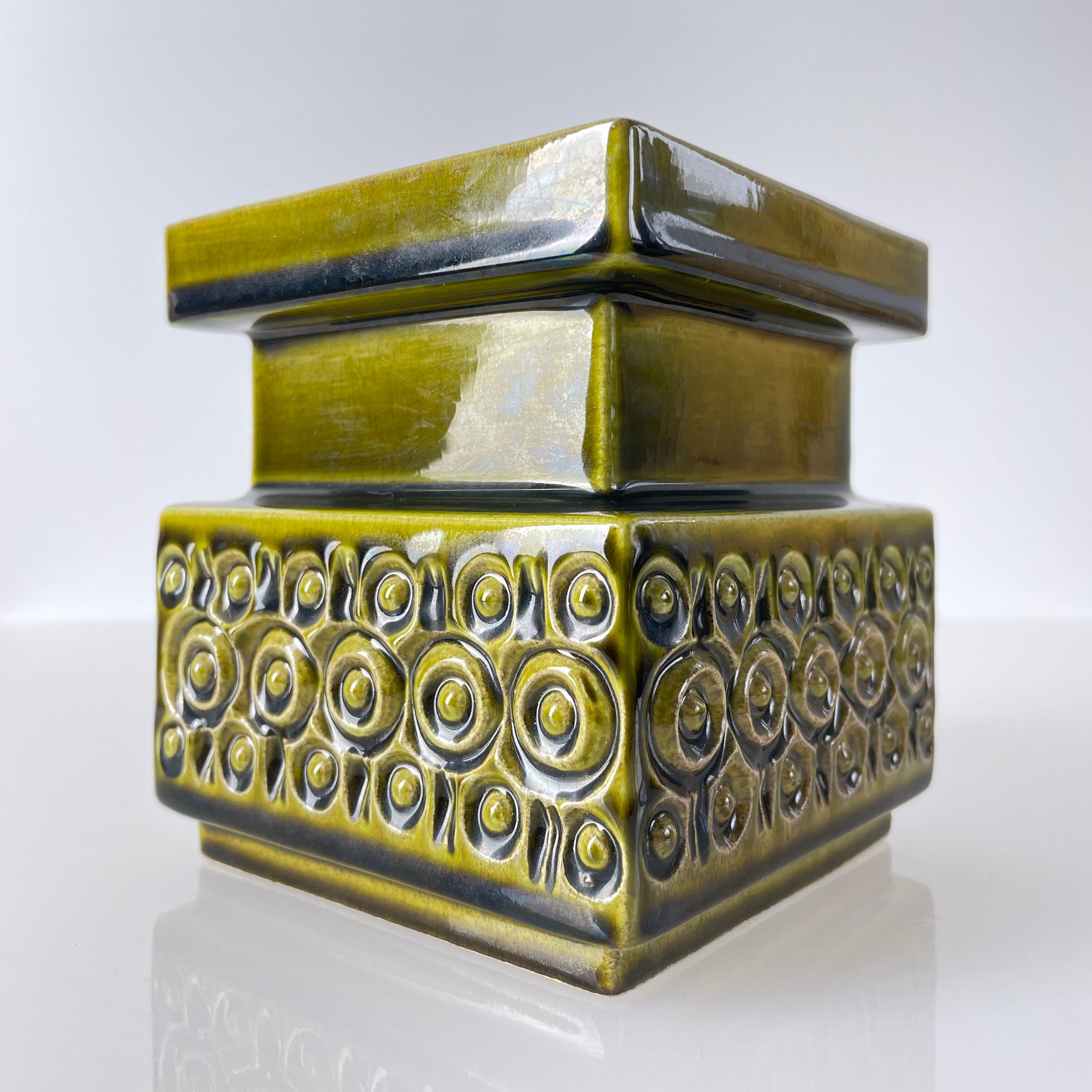 Dekorativer Keramik-Kerzenhalter, hergestellt von JK Kunstkeramik (W.Deutschland) in den späten 60er bis Mitte der 1970er Jahre. Mit einem Reliefmuster und olivgrüner Glasur. Herstellerkennzeichen auf dem Sockel.