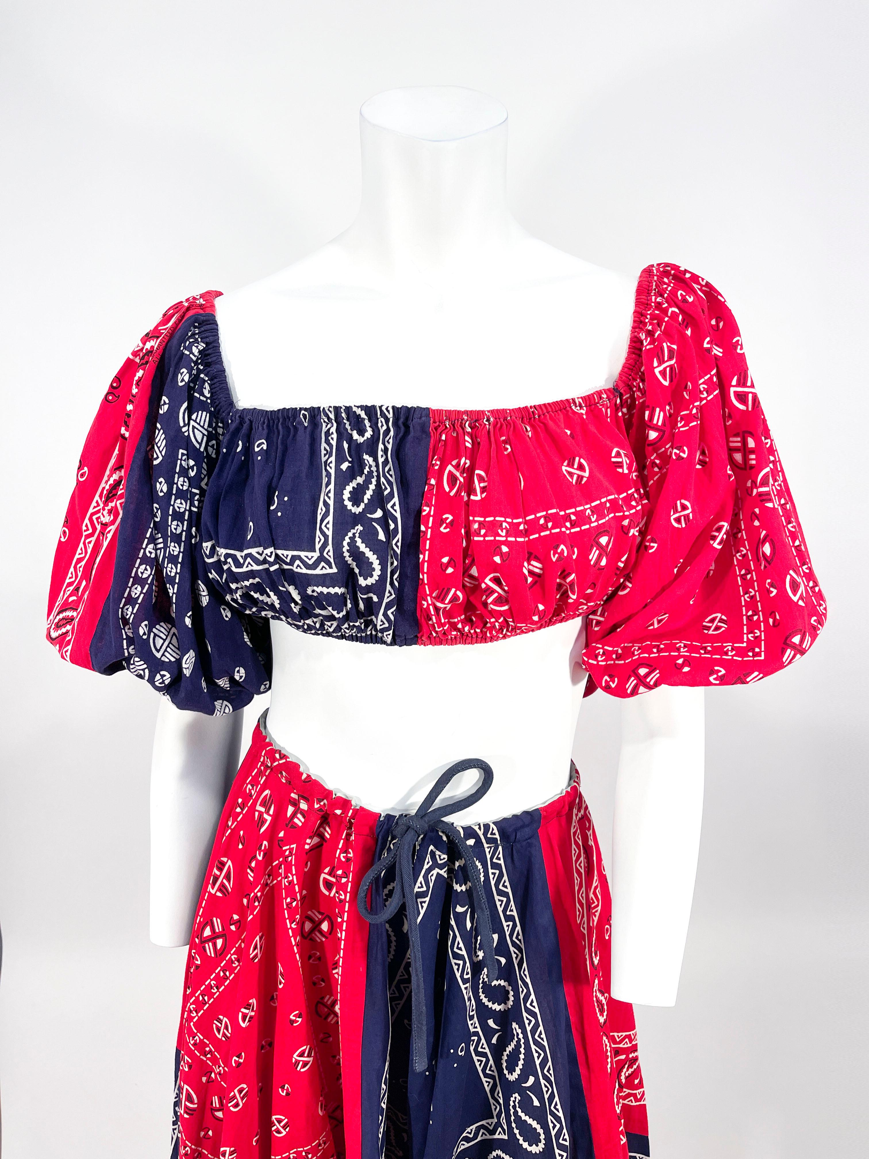 Late 1960s to early 1970s handmade red and blue bandana two-piece set. The peasant style top features full puff sleeves that may be worn on or off the shoulder due to the elasticated hems. The skirt has a handkerchief hem and a corded waist tie to