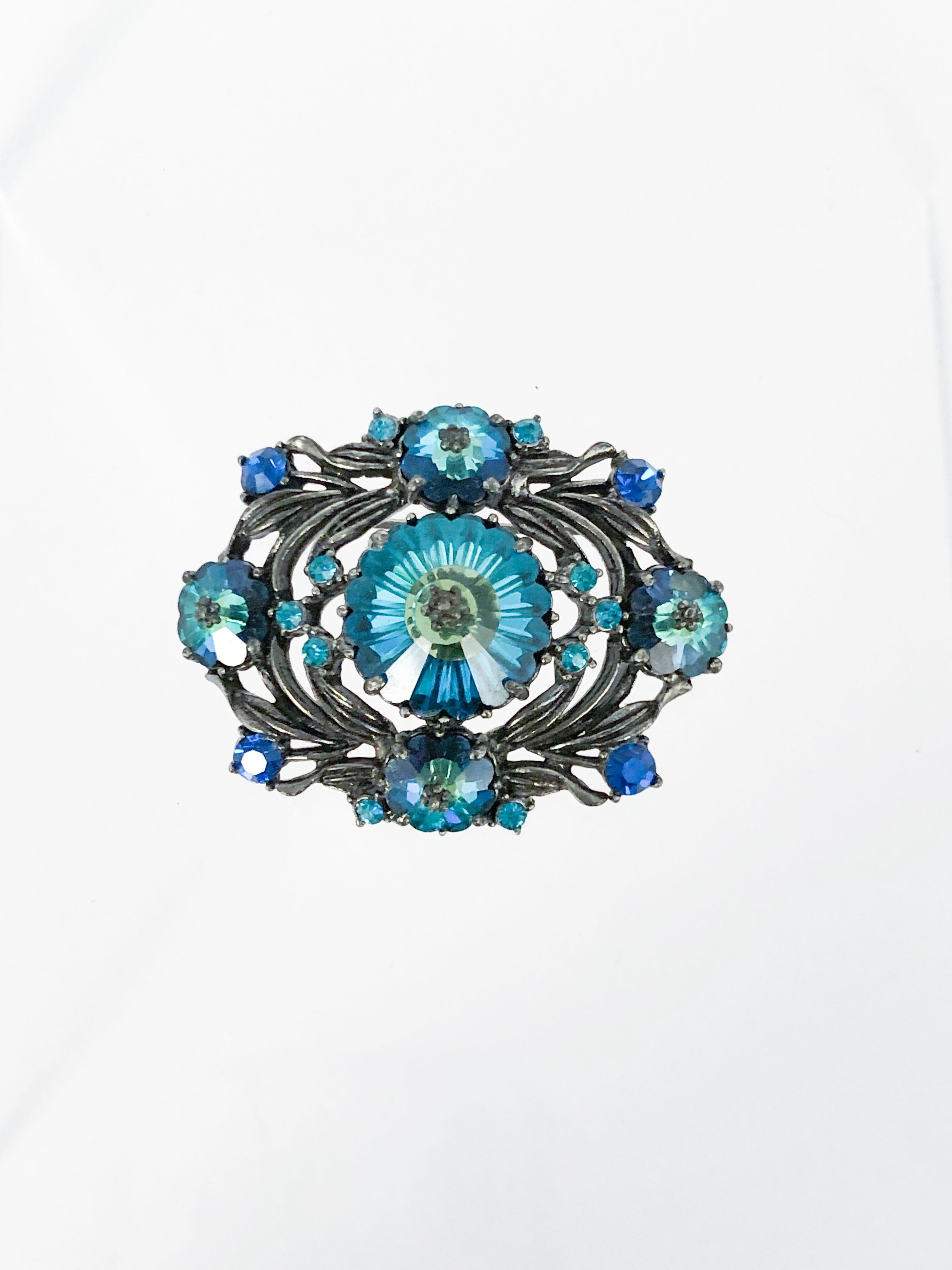 Late 1960s/Early 1970s Weiss brooch with multi-tones of Blues and green rhinestones. The stones are set in a silver-toned metal that is stylistically tarnished for a bohemian look. The back has a standard brooch pin and shows the Weiss hallmark.