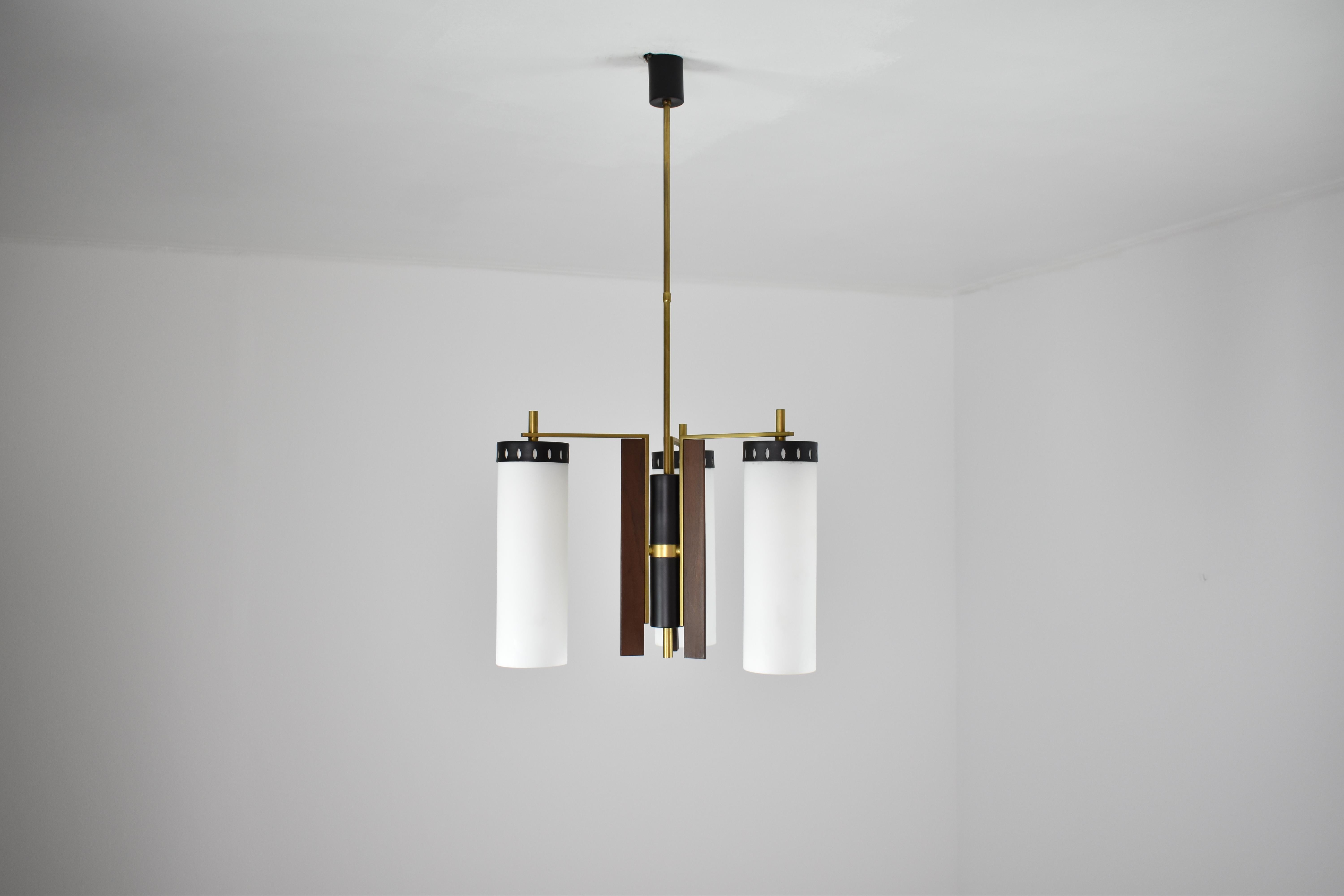 A beautiful 1960s Italian three-light pendant composed of long milk glass circular structures attached with black steel perforated sheets. The sophisticated structure is designed of brass, wooden panels and steel. 
The warmth of wood, the