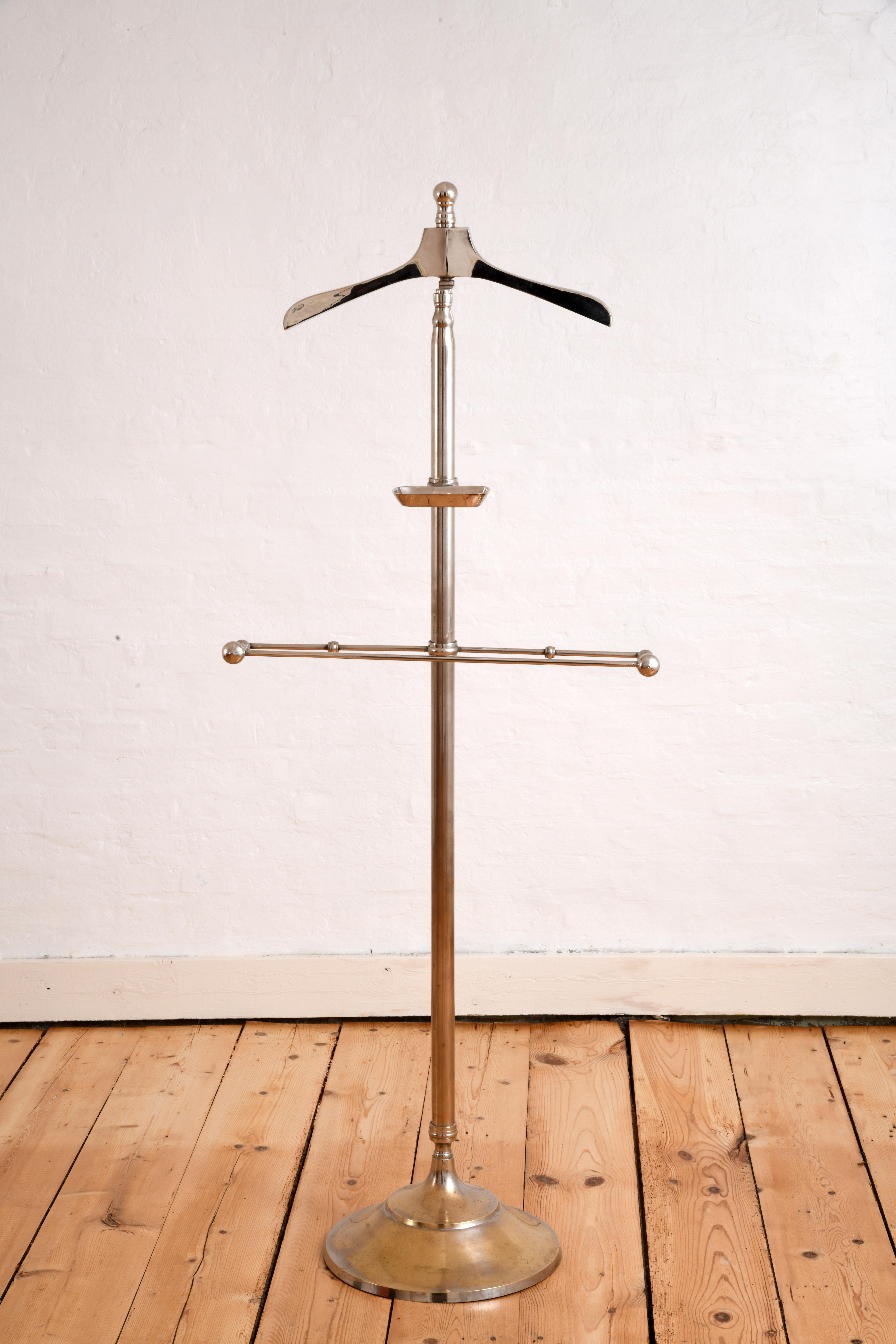 Valet stand for the bedroom or bathroom. Made of chrome-plated brass, it features a hanger for shirts and jackets, a trouser rack and a pocket for watches, lighters, coins, etc. The rack and pocket are height-adjustable and can be rotated on the