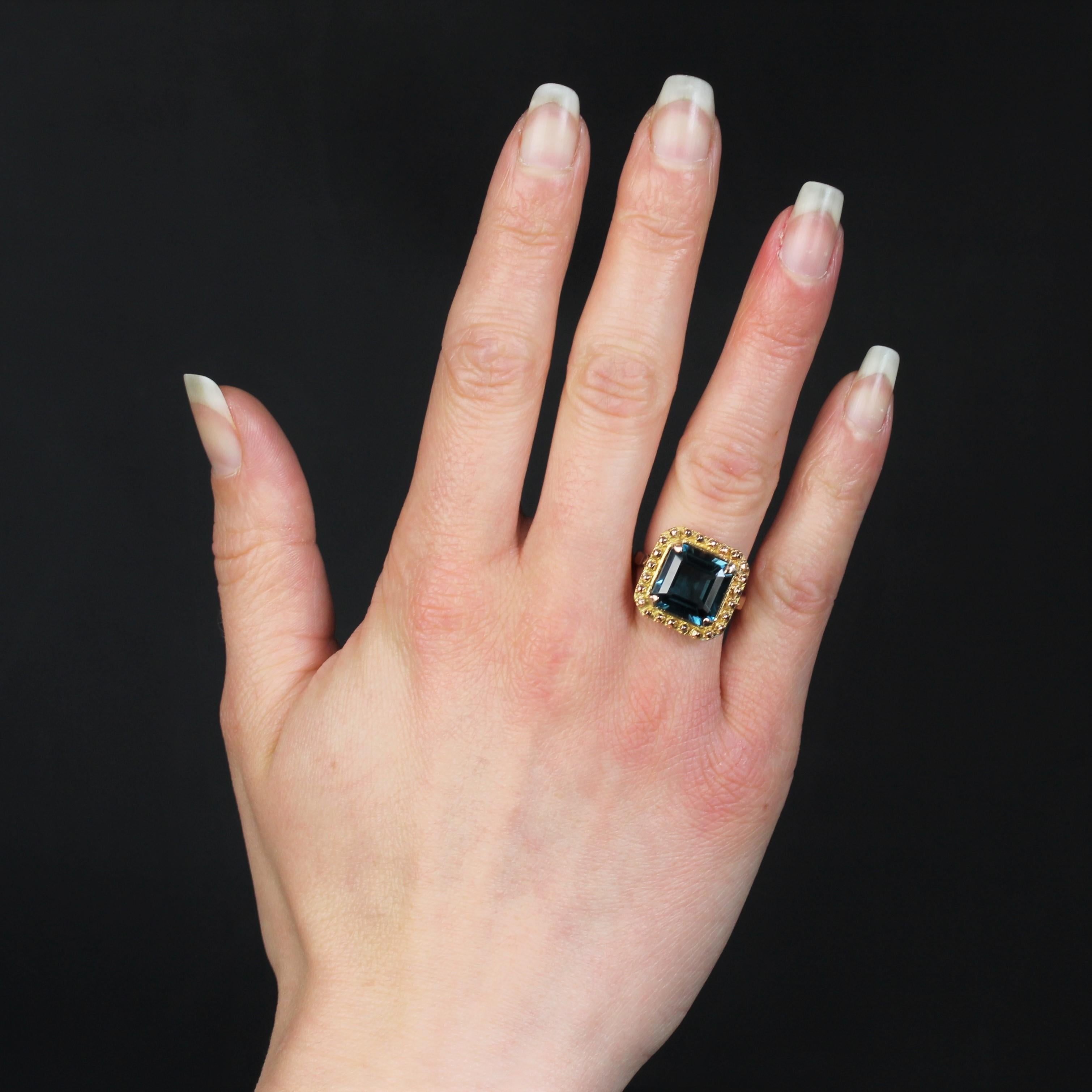 Ring in 18 karat yellow gold.
Retro square shape ring, it presents a decoration formed of small rose gold nails and is centered of a blue topaz retained with 4 flat claws in the angles. The basket is openworked.
Total weight of the topaz : 7.30