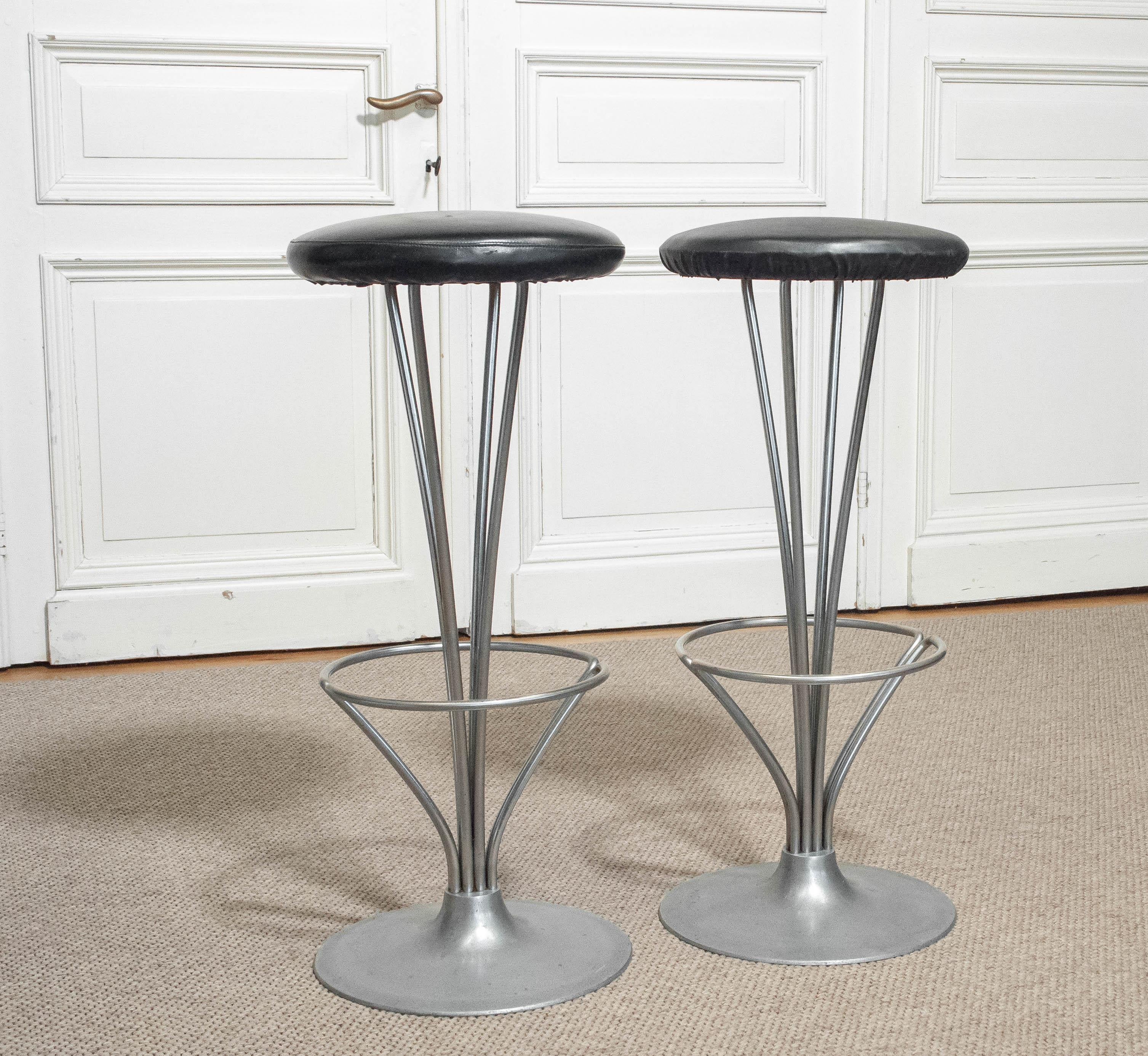 Paire de tabourets de bar conçus par Piet Hein pour Fritz Hansen, Danemark, années 1960. Dotés d'une base sculpturale en aluminium à la forme fuselée élégante et de repose-pieds intégrés, ces tabourets sont surmontés d'assises rondes rembourrées en