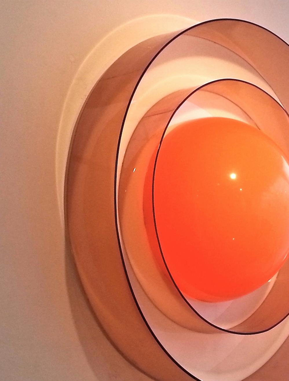 French, 1960s
large, sculptural wall light with domed orange acrylic 'egg yolk' concealing the lighting element, surrounded by two concentric smoke perspex bands.
(2 identical additional wall lights are available). 