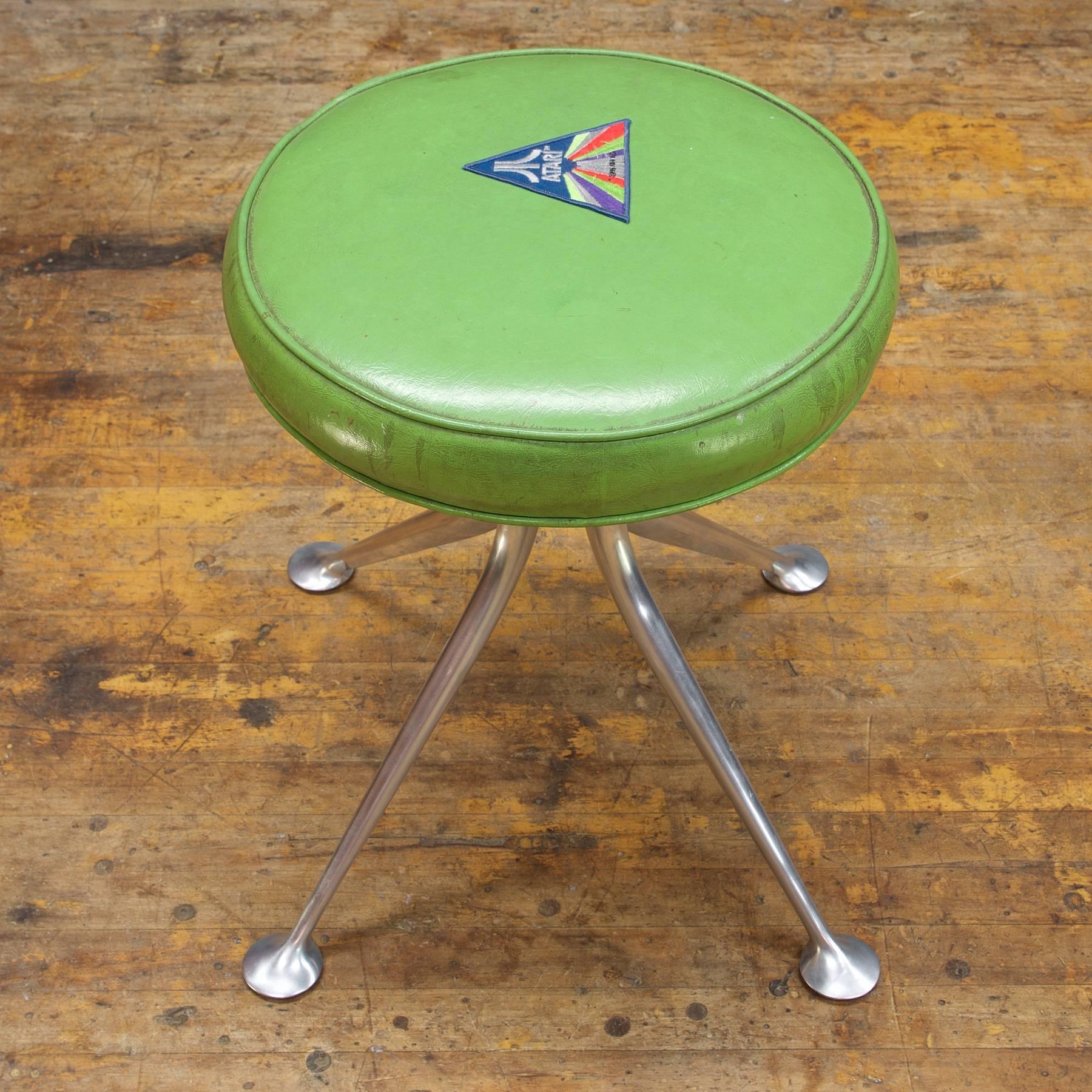 A rare original first run Alexander Girard designed model no.66308 stool, manufactured by Herman Miller, in cast and milled aluminium. The round seat cushion is heavily patinated green vinyl, repaired with a mid-1970s Atari patch.