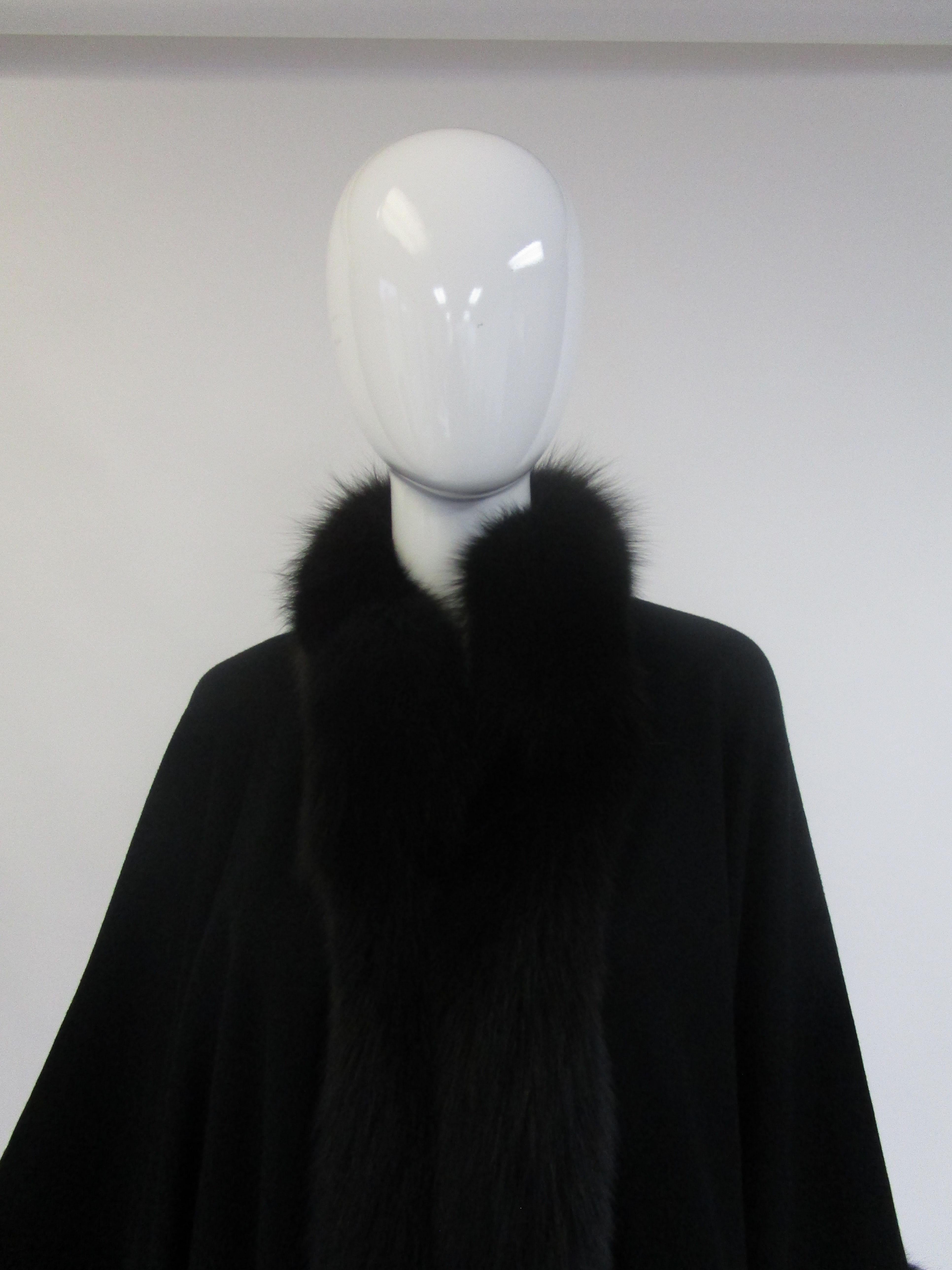 
Wrap up in this incredibly warm and striking cape from Alixandre!
It consists of a wool blend felt body with undulating black fox fur trim. The way it drapes over the wearer almost gives the appearance of sleeves. The back of the cape drapes
