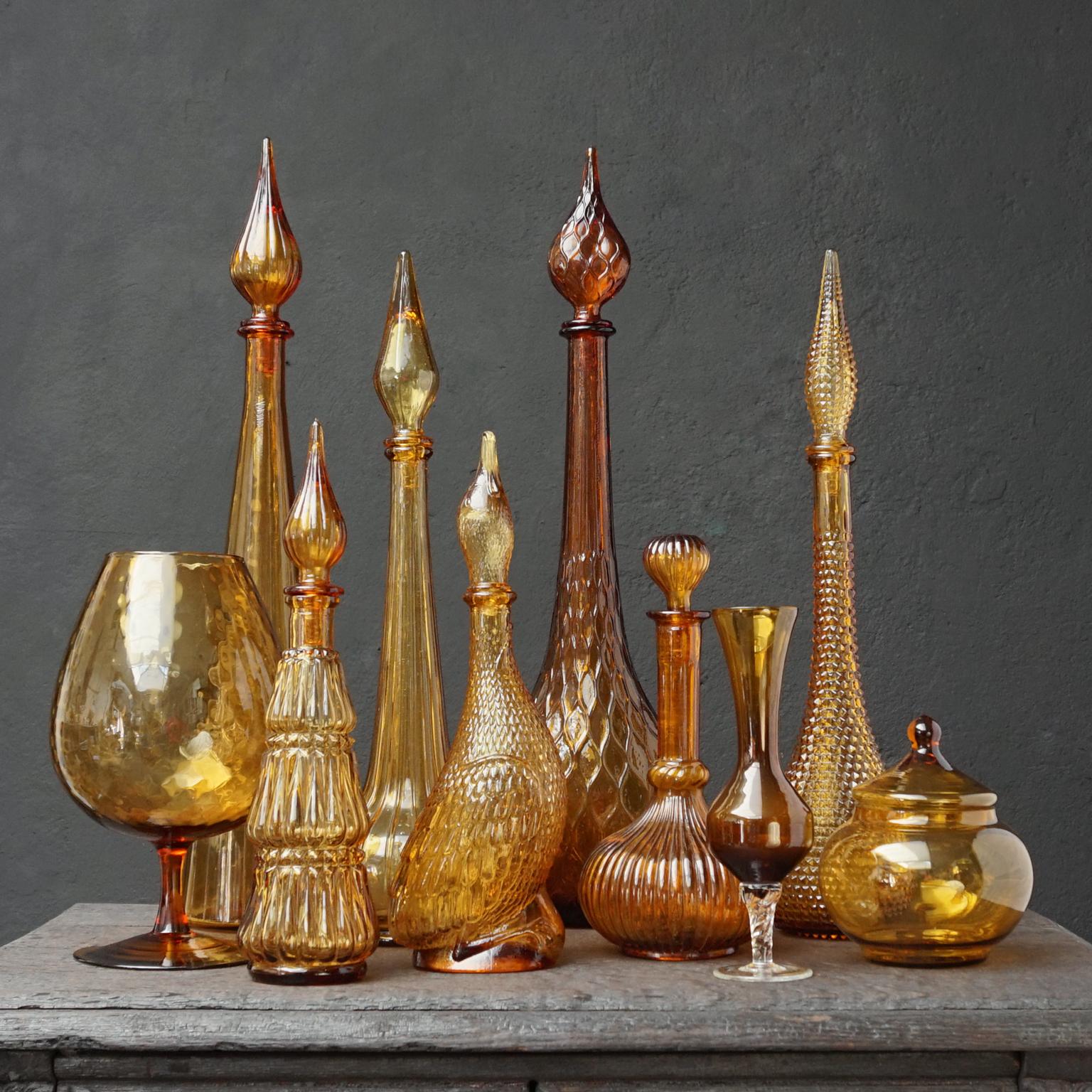 Very decorative amber brown yellow set of ten different size and colour Italian glass.
Seven pressed genie bottles and three blown clear glass items; a brownish yellow vase, a large cognac glass and a bonbon or candy jar.

Mention Italian glass and