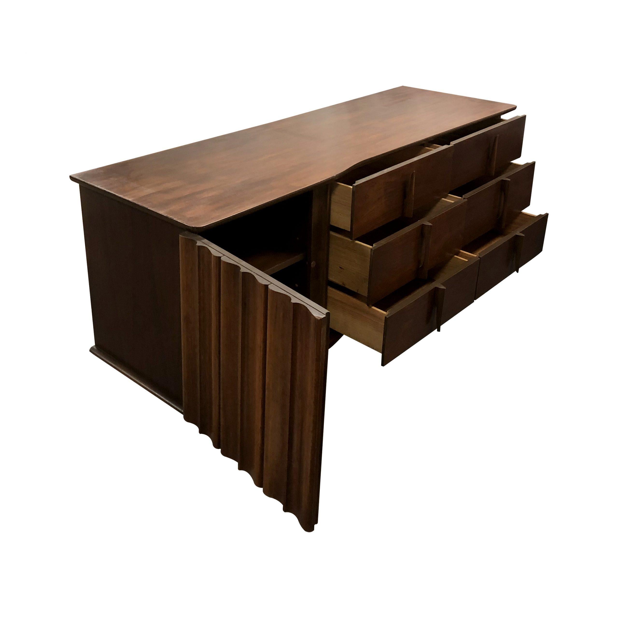 An American 1960s Brutalist sculptural walnut credenza or sideboard. This elegant sideboard has a curved carved door on the left hand side which is split into three vertical sections which contrasts with the straight lines of the six drawers on the