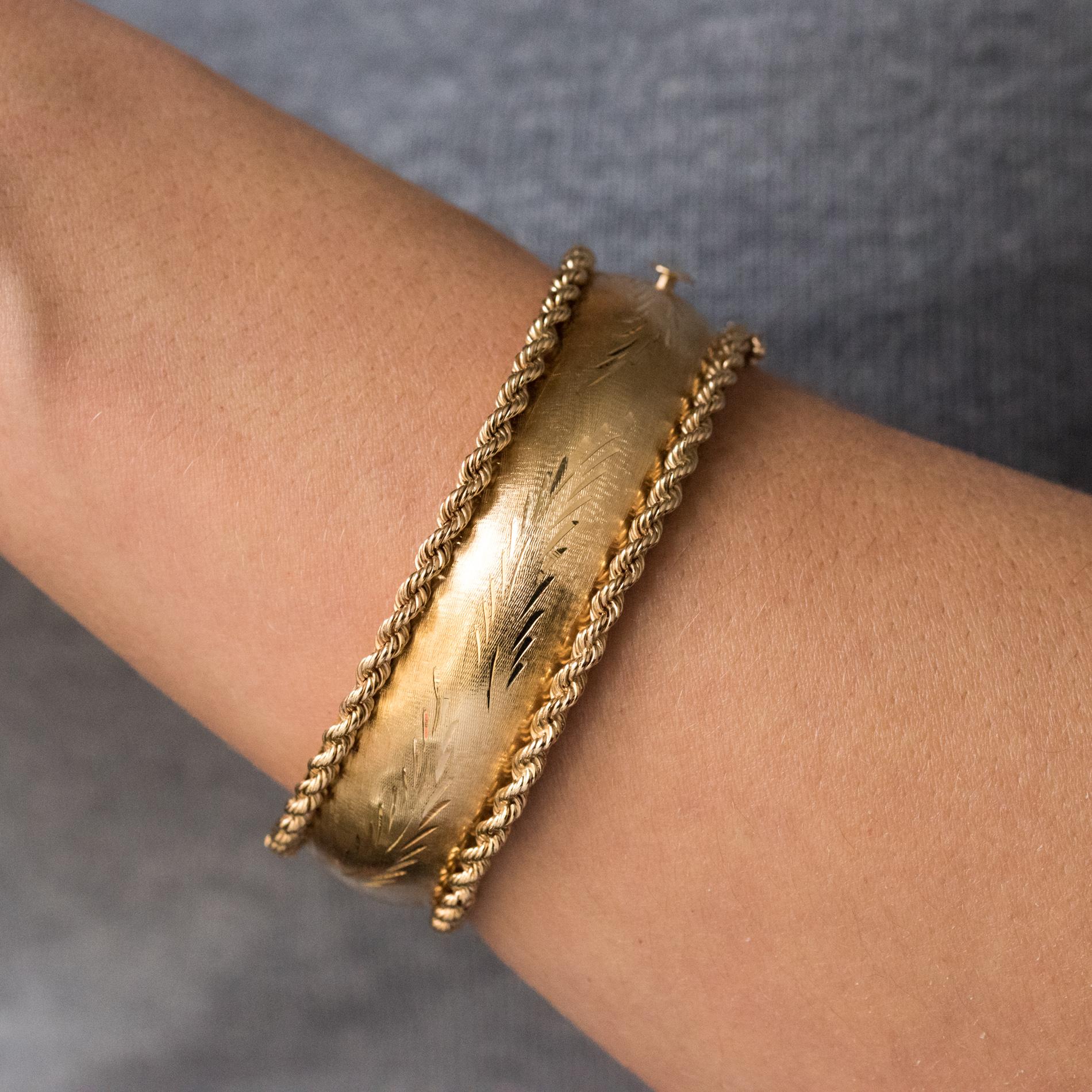 Bracelet in 14 karats yellow gold, shell hallmark.
Rigid, this retro bracelet is chiseled all around with a plant motif on amati background and bordered on both sides of a twist. It is opening on one side. The clasp is ratchet with a security