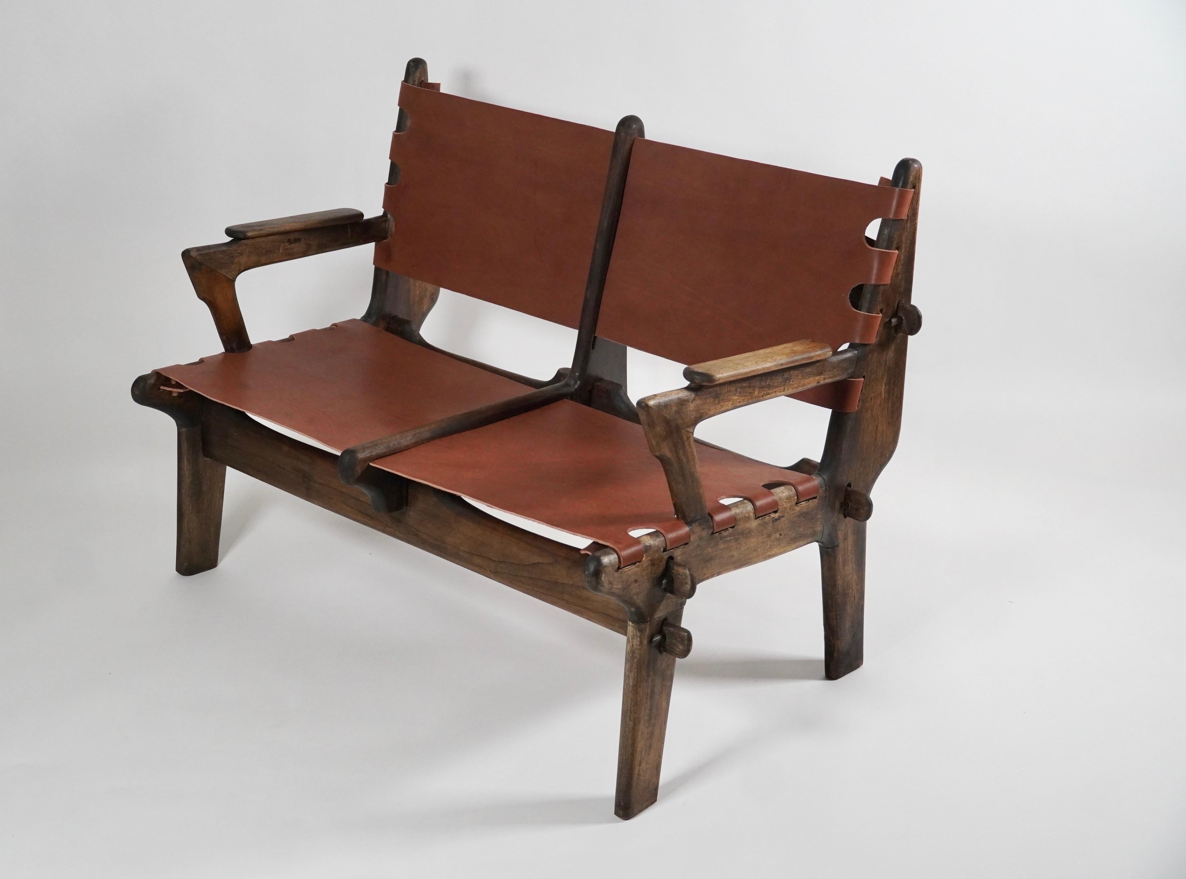 Settee by South American designer Angel Pazmino for Muebles de Estilo of Ecuador circa 1960s. Entirely hand made out of the indigenous tropical woods of Ecuador with a thick russet colored latigo leather upholstery. Held together via joints and a