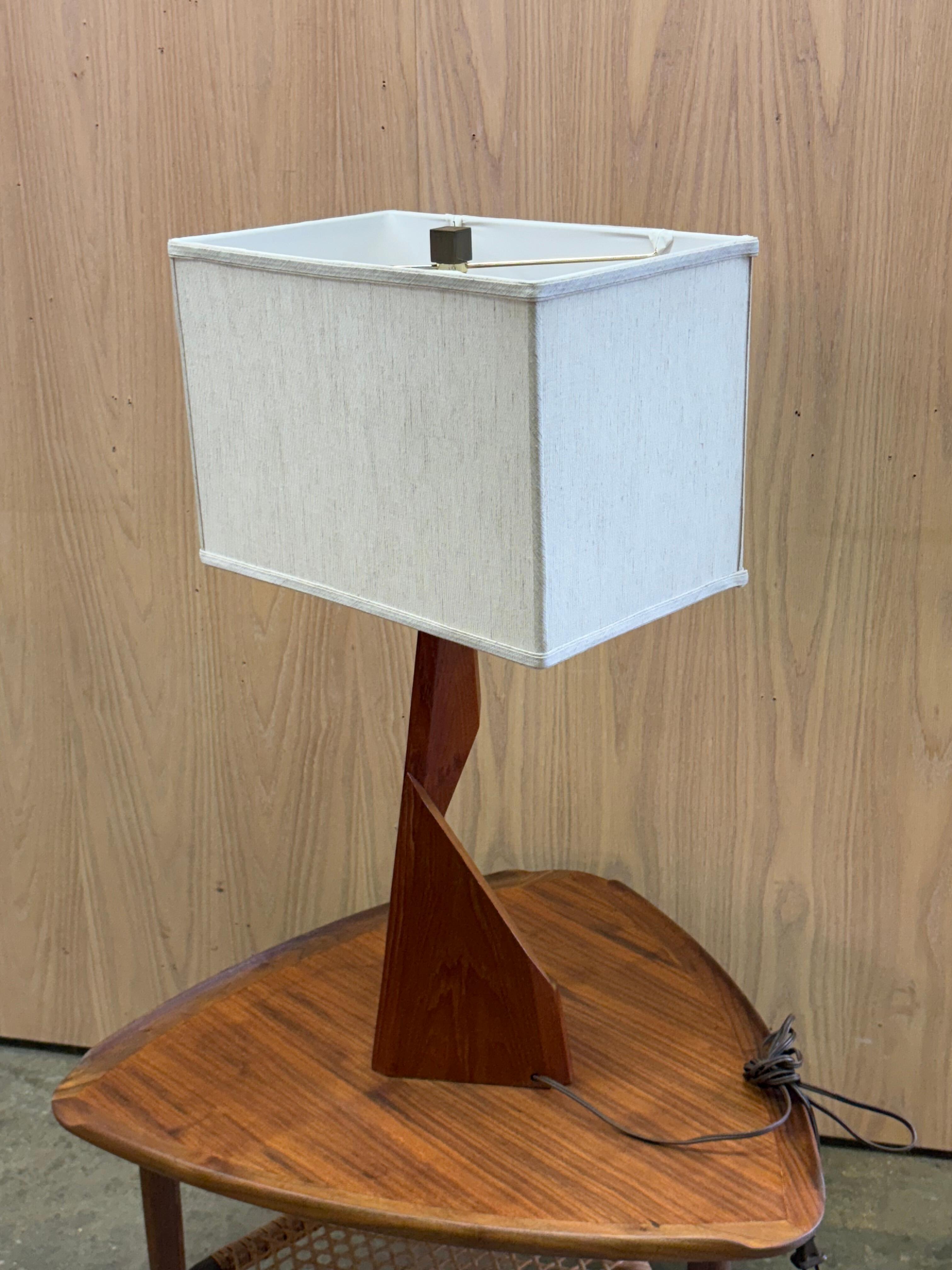 A sculptural 1960s solid teak table lamp, crafted in Canada with the same architectural language as the matching floor lamp. Its sharp, folded planes and carved geometric silhouette create a striking presence while remaining warm and refined in