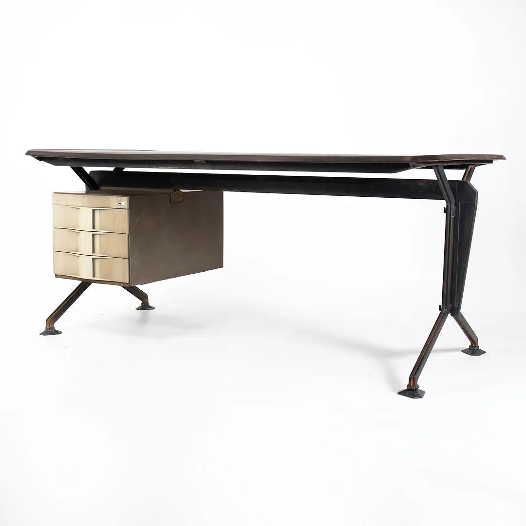 This is an Arco desk, designed by Studio B.B.P.R for Olivetti Sintesis in 1963. The piece was manufactured in Italy in the 1960s. The frame and base are made of iron, and it has a case on the left hand side containing 3 drawers. This silhouette is